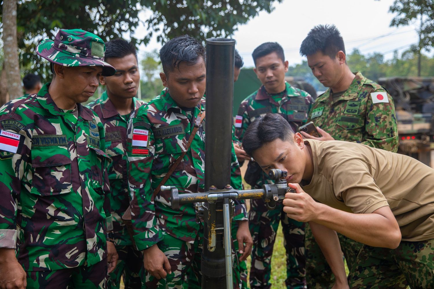 Soldiers from multiple nations observe mortar assembly instruction during a joint military training exercise.