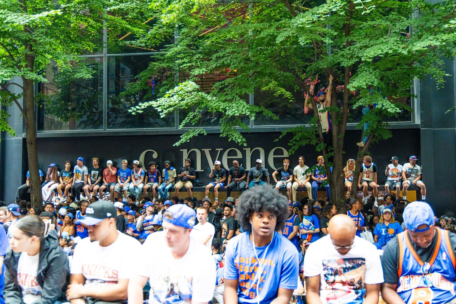 Large crowd gathered outside Convene venue, fans wearing blue team jerseys under lush green trees on a sunny day.