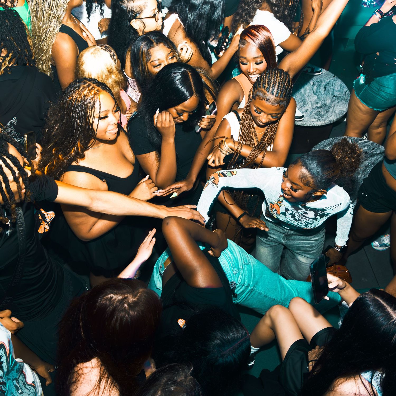 A lively group of young women dancing together at a nightclub party in a crowded venue.