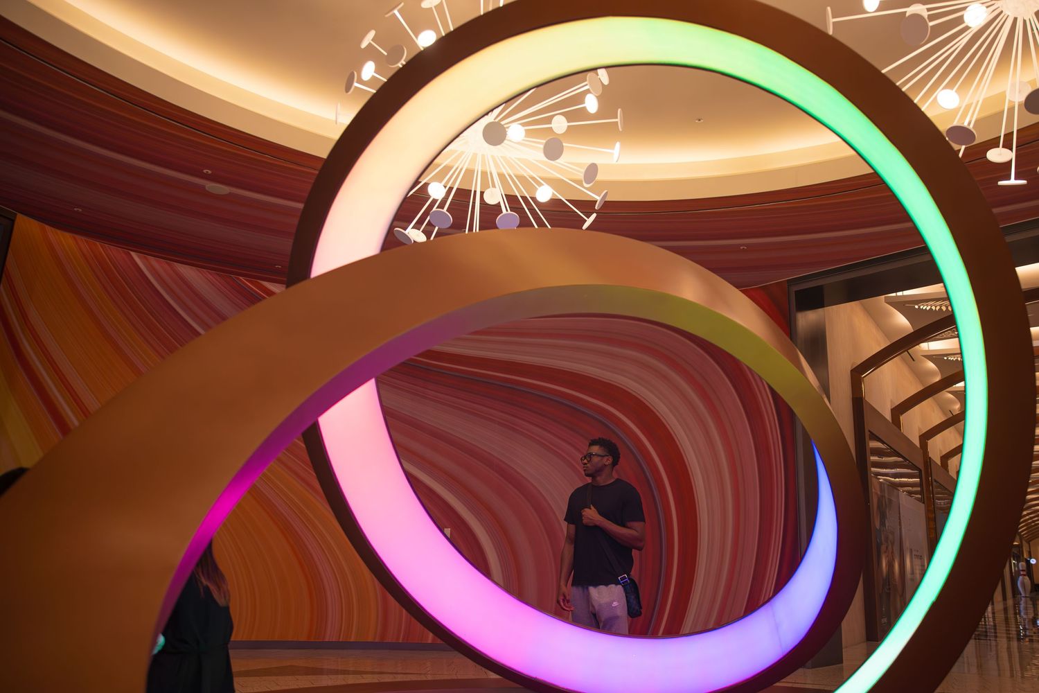 Man standing inside colorful illuminated spiral art installation in a modern luxury interior space.