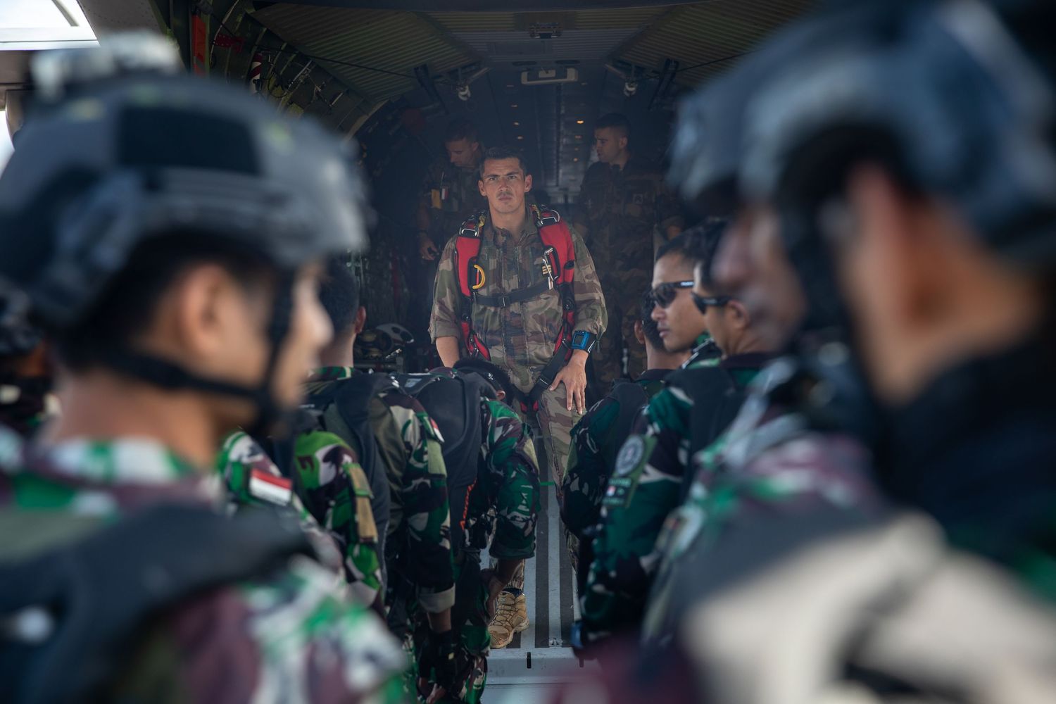 A soldier briefs multinational military troops inside a military aircraft before a parachute jump operation.