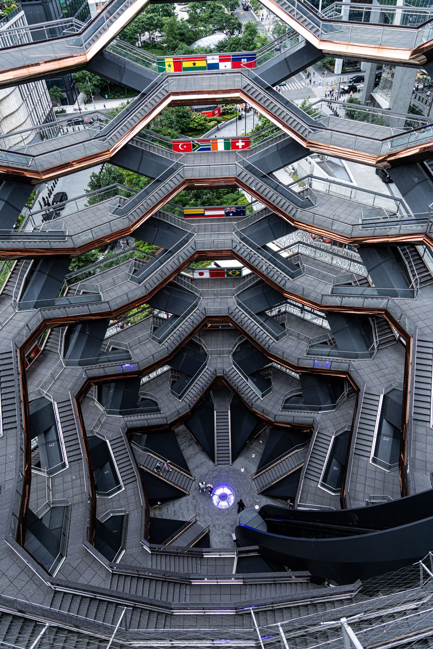 Aerial view looking down into The Vessel at Hudson Yards NYC, showing intricate honeycomb staircase structure with international flags.