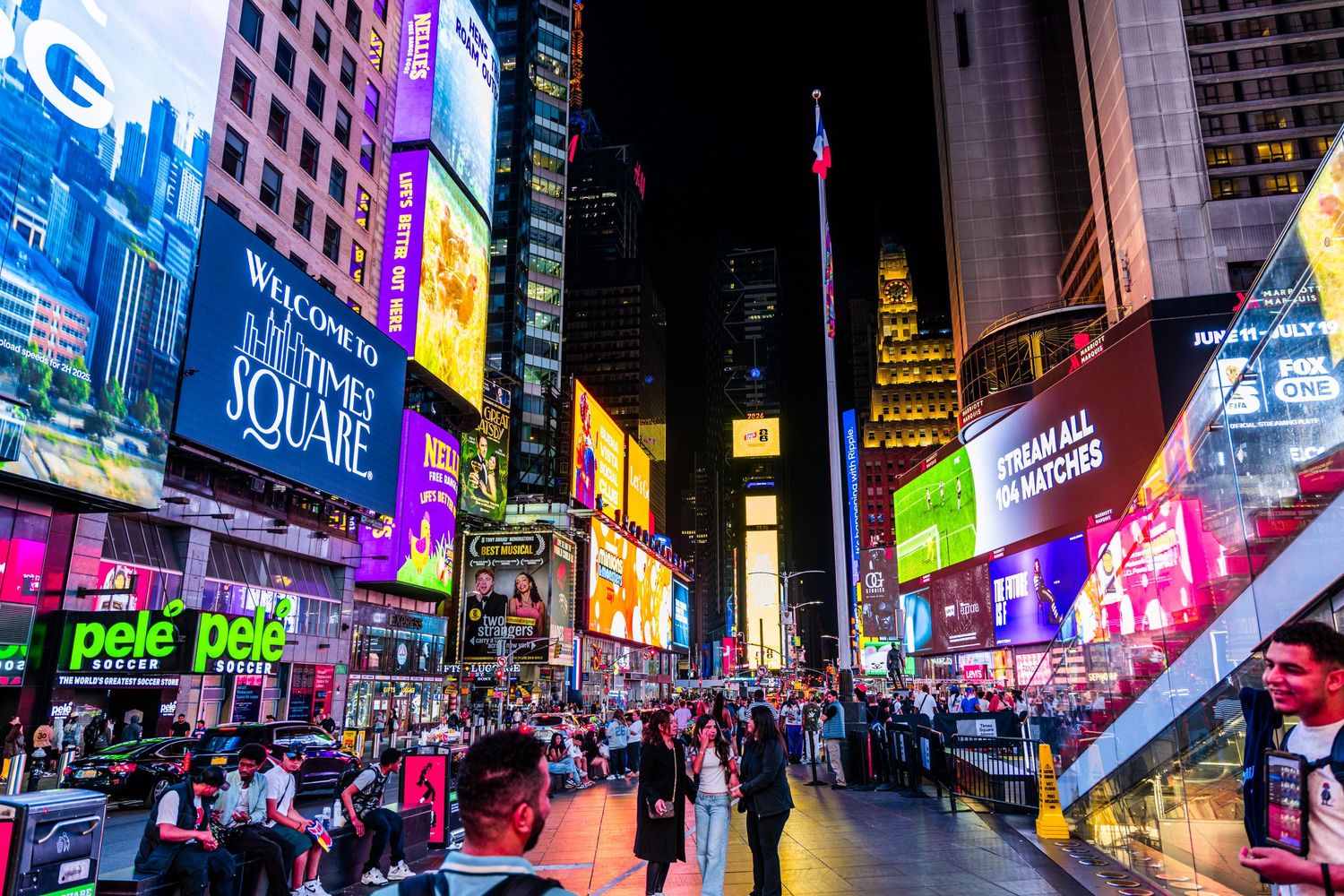 Vibrant Times Square at night with colorful billboards, crowds of tourists, and iconic NYC skyscrapers illuminated.