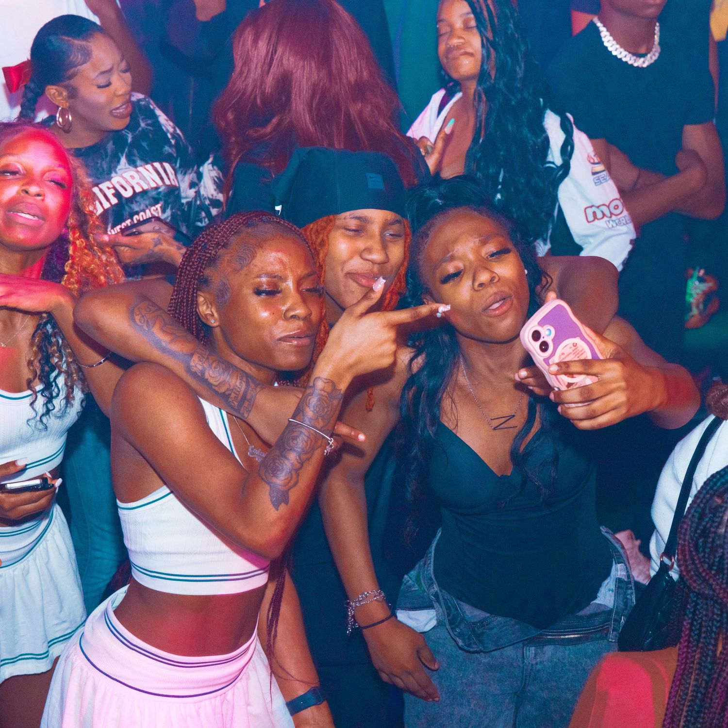 Group of young women posing together and smiling at a lively indoor party or club event.