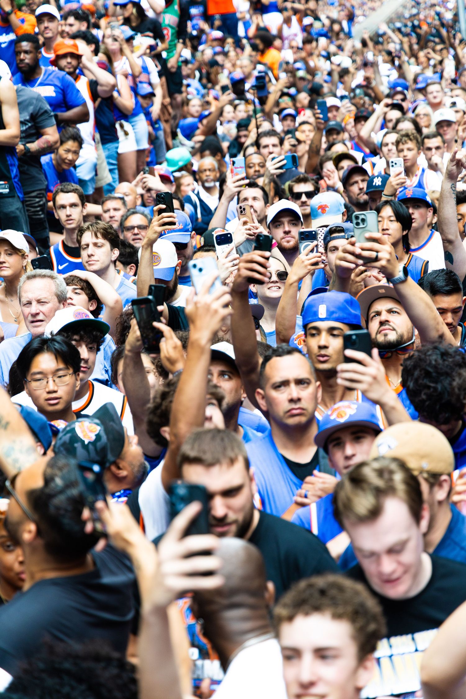 Large crowd of New York Knicks fans taking photos with smartphones at an outdoor rally event.