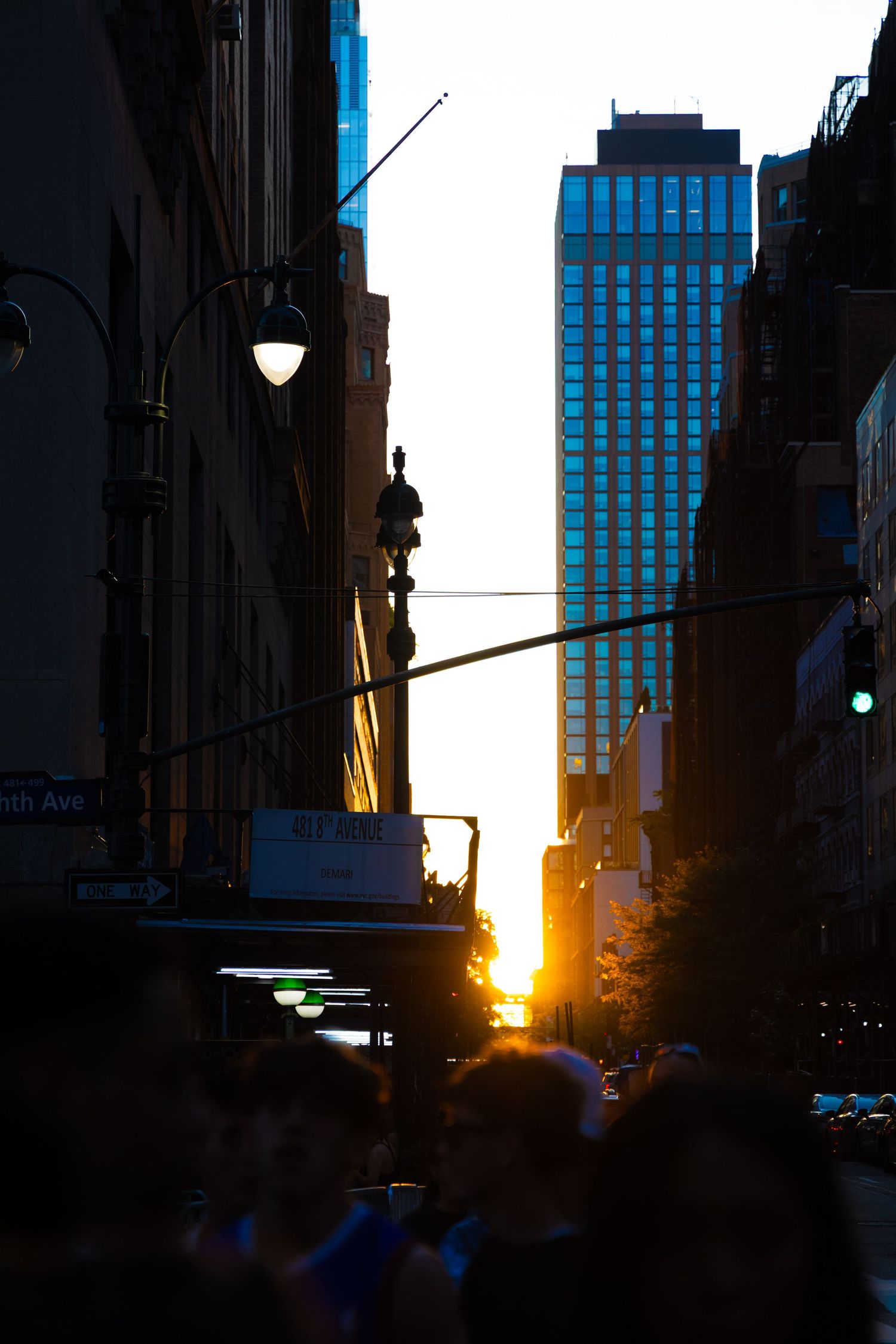 Golden sunset light illuminates a crowded New York City street between tall buildings during Manhattanhenge.