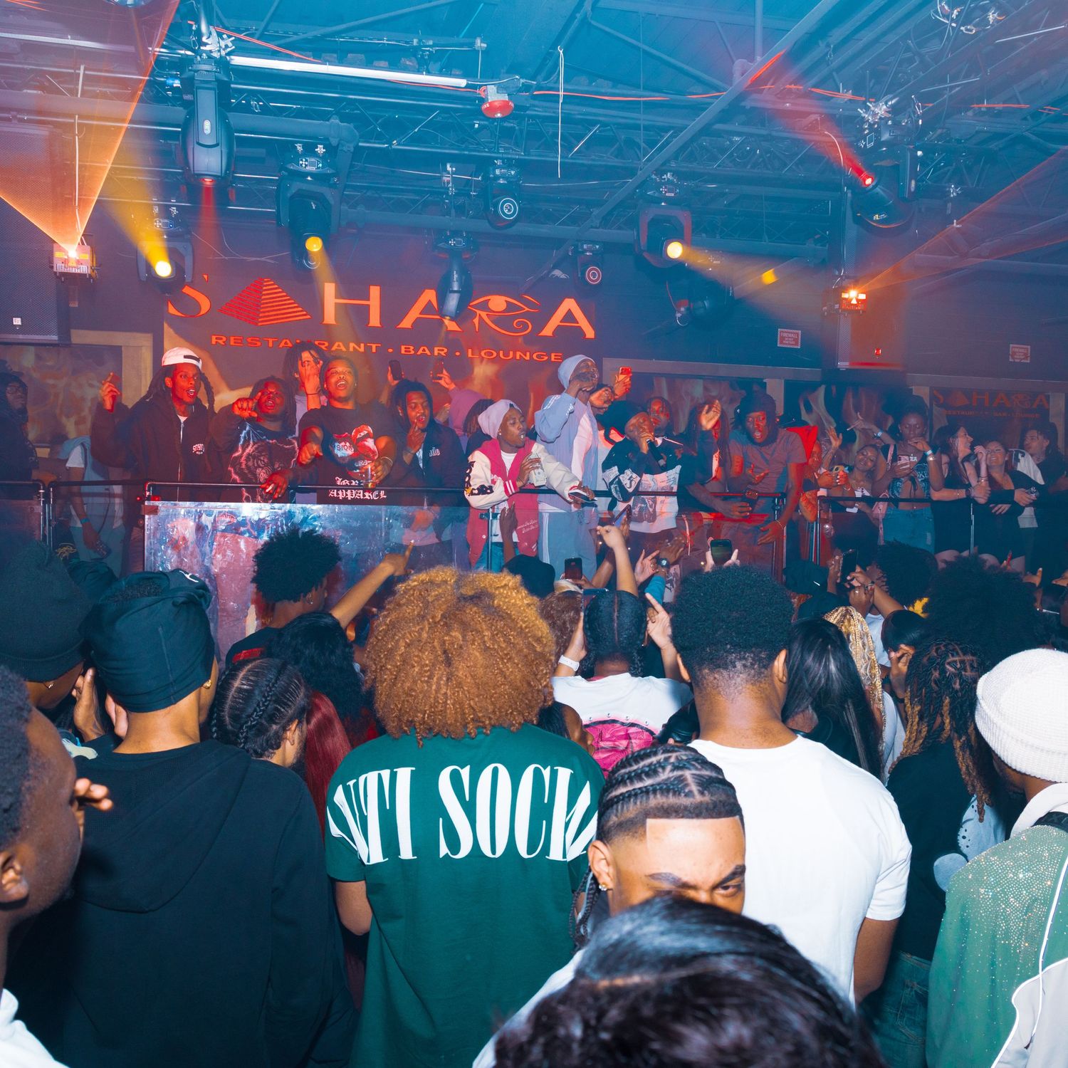 Energetic crowd dancing at Sahara nightclub with vibrant stage lighting and performers on stage.