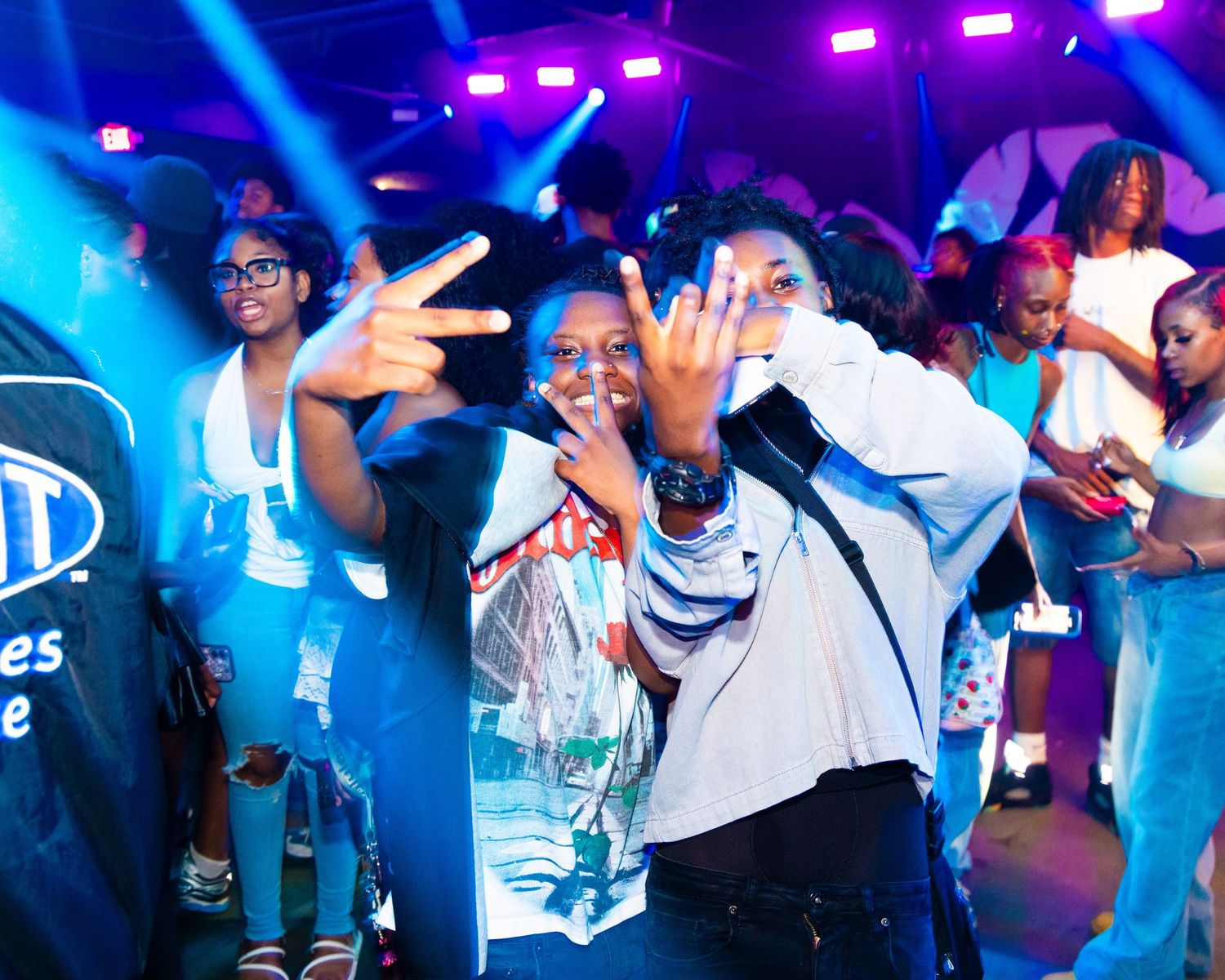Young people dancing and posing at a vibrant nightclub event with colorful stage lights.