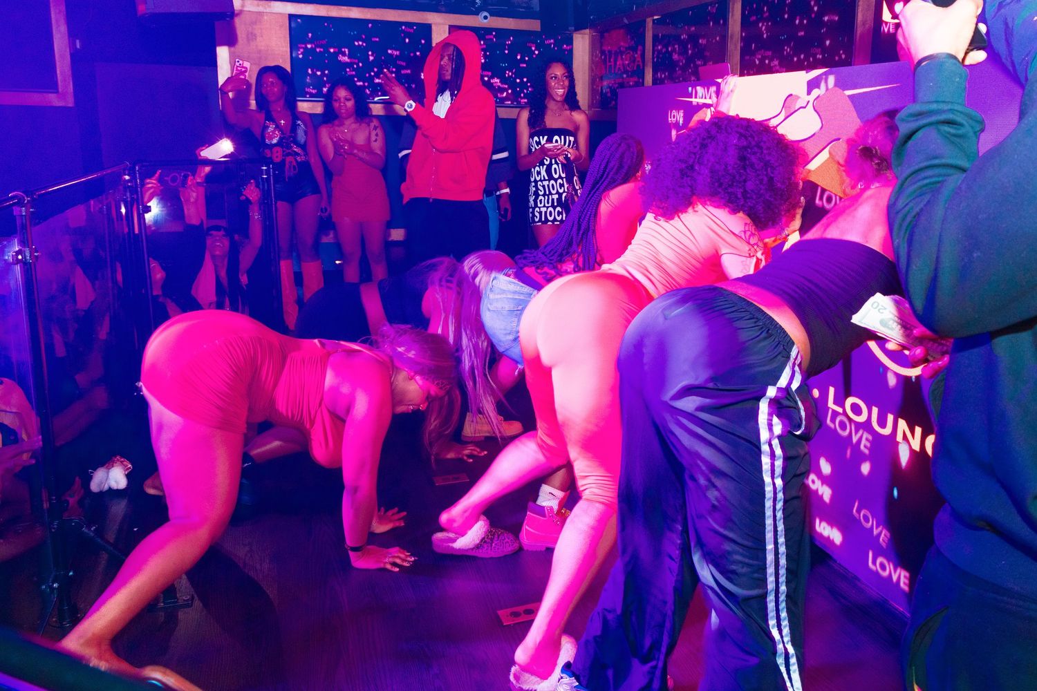 Group of people dancing and partying at a nightclub lounge with colorful purple and pink lighting.