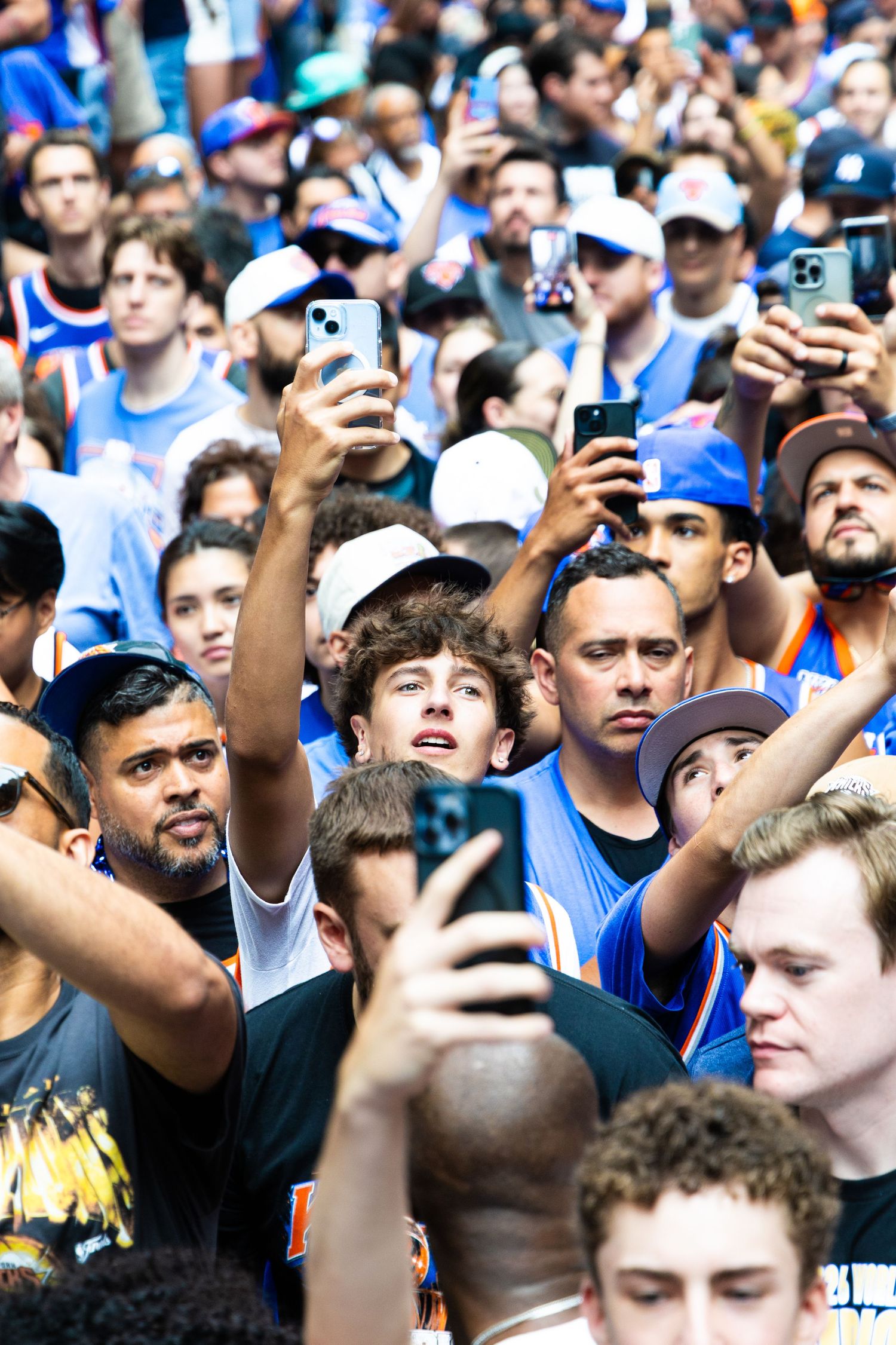 Large crowd of New York Knicks fans holding up smartphones at an outdoor event, wearing team jerseys and caps.