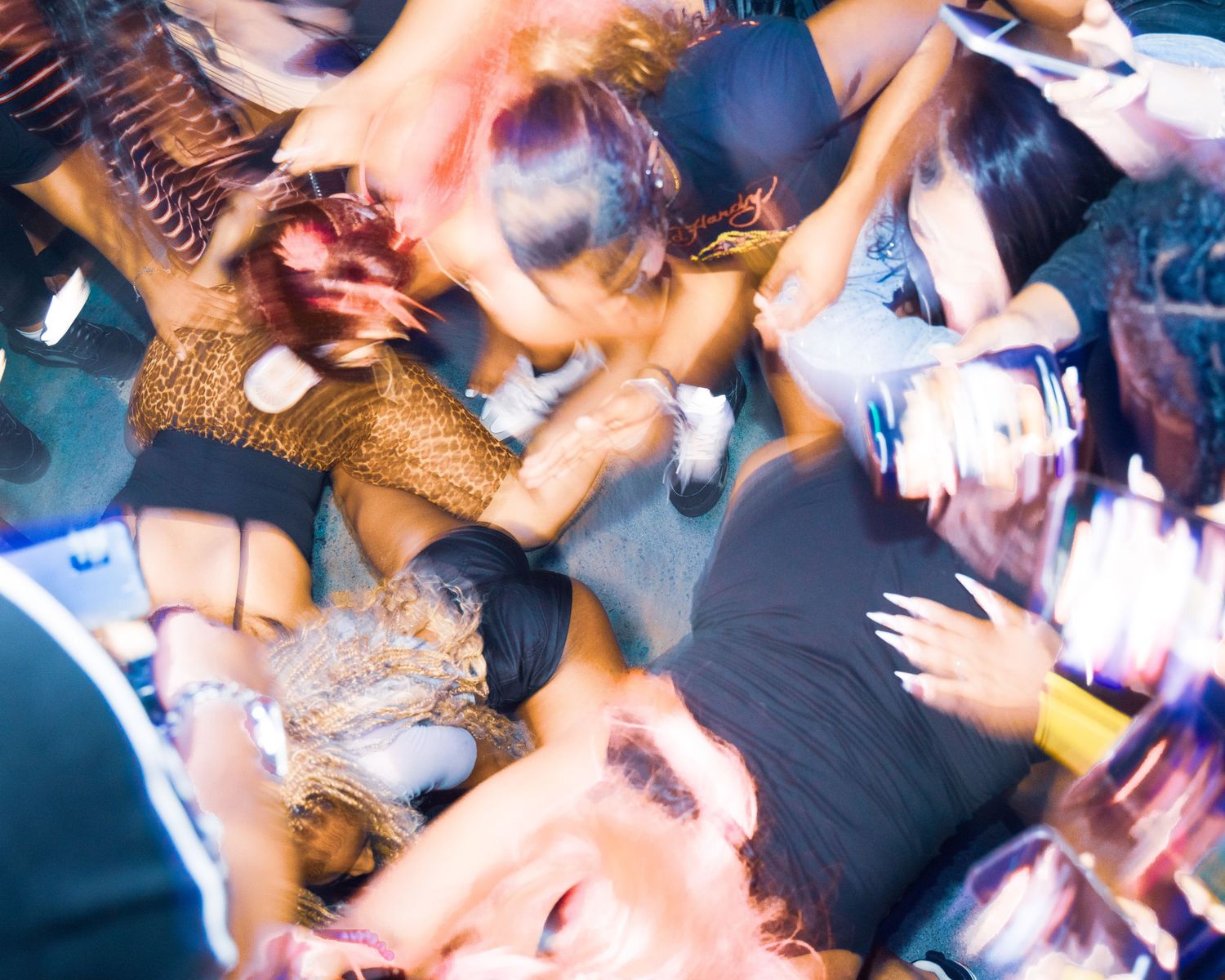 Aerial view of a lively crowd dancing at a nightclub party with colorful lighting and motion blur.