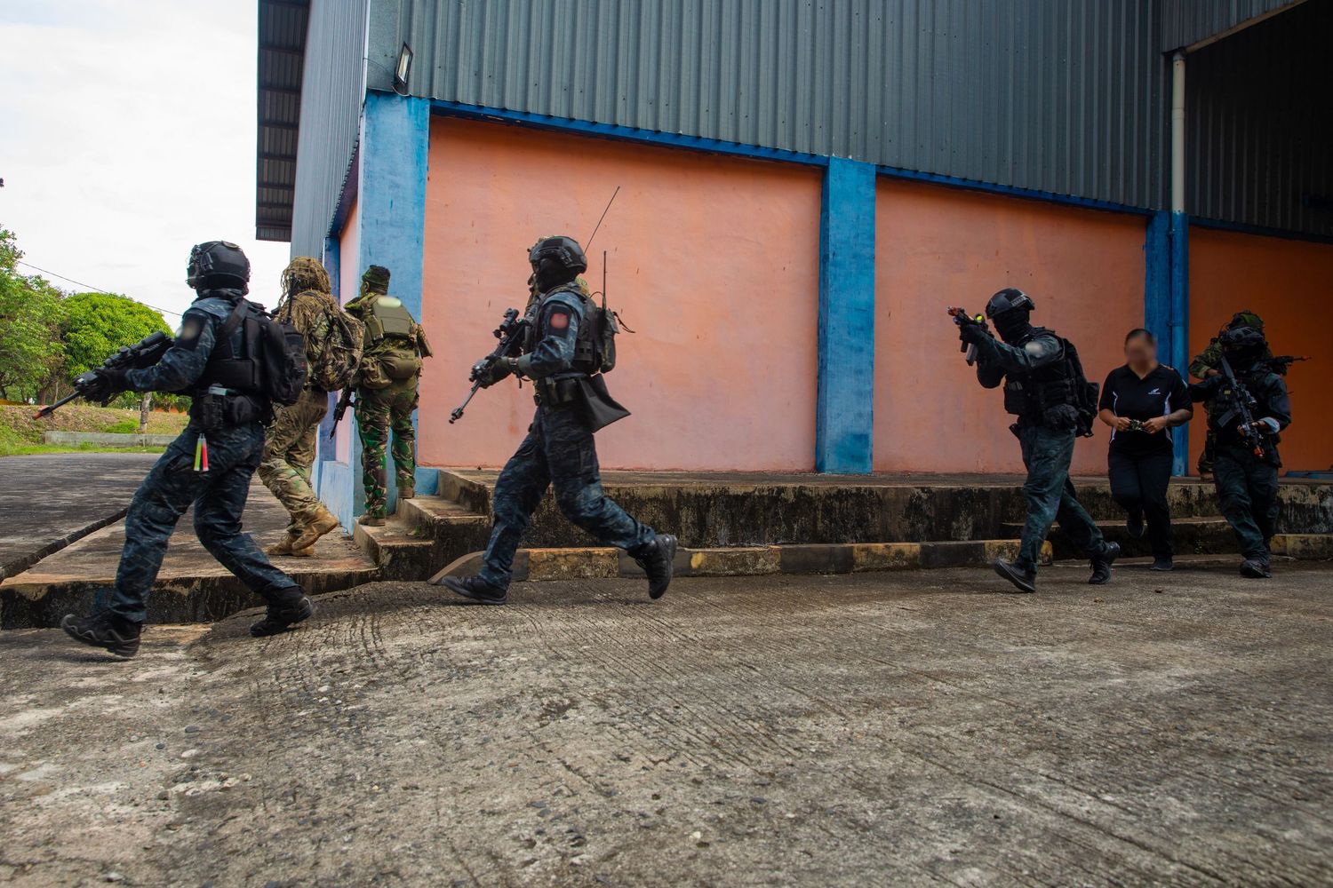 Tactical military team in black gear running alongside building during special operations training drill.