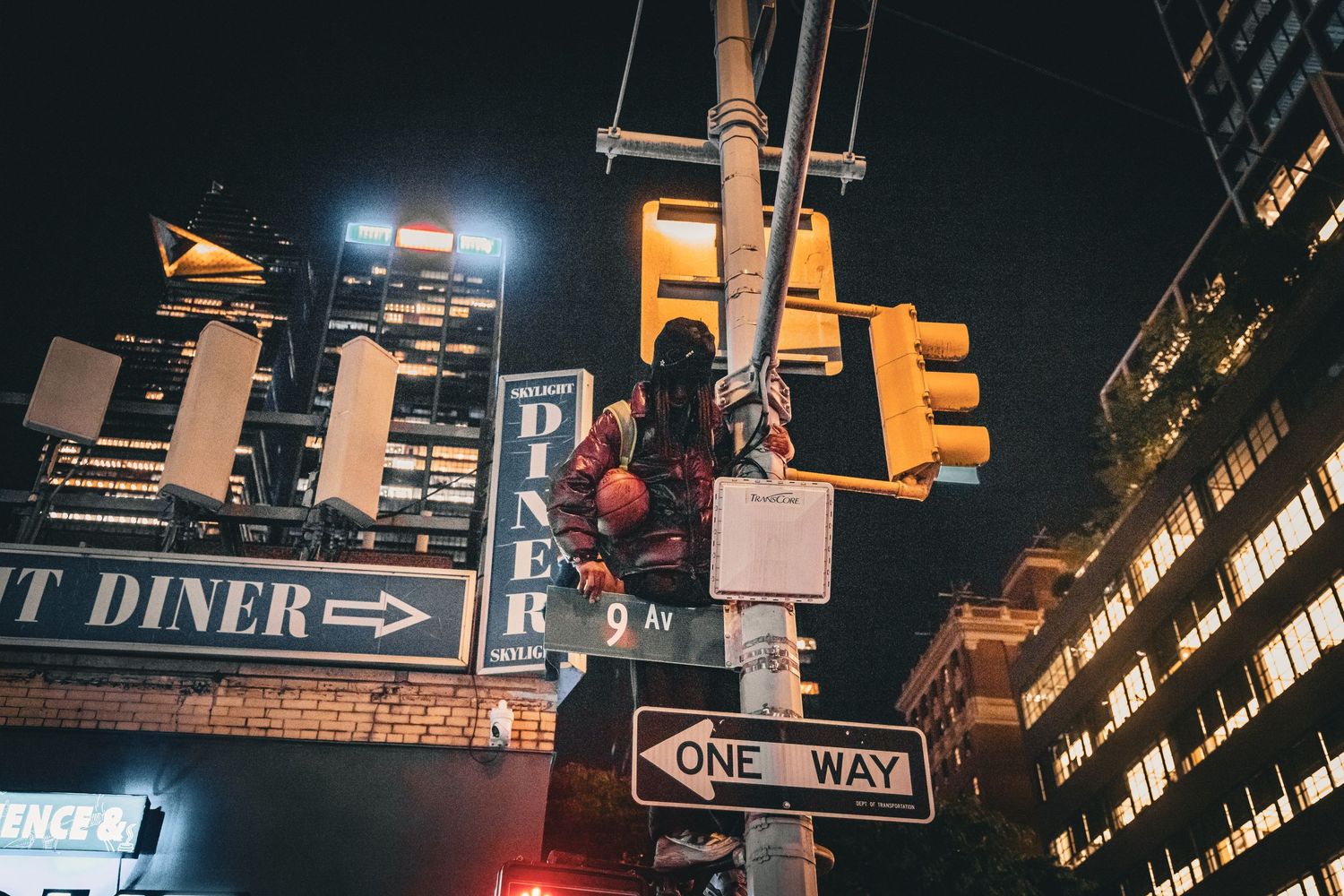 Night cityscape with traffic lights, one way sign, and diner sign illuminated by city lights.