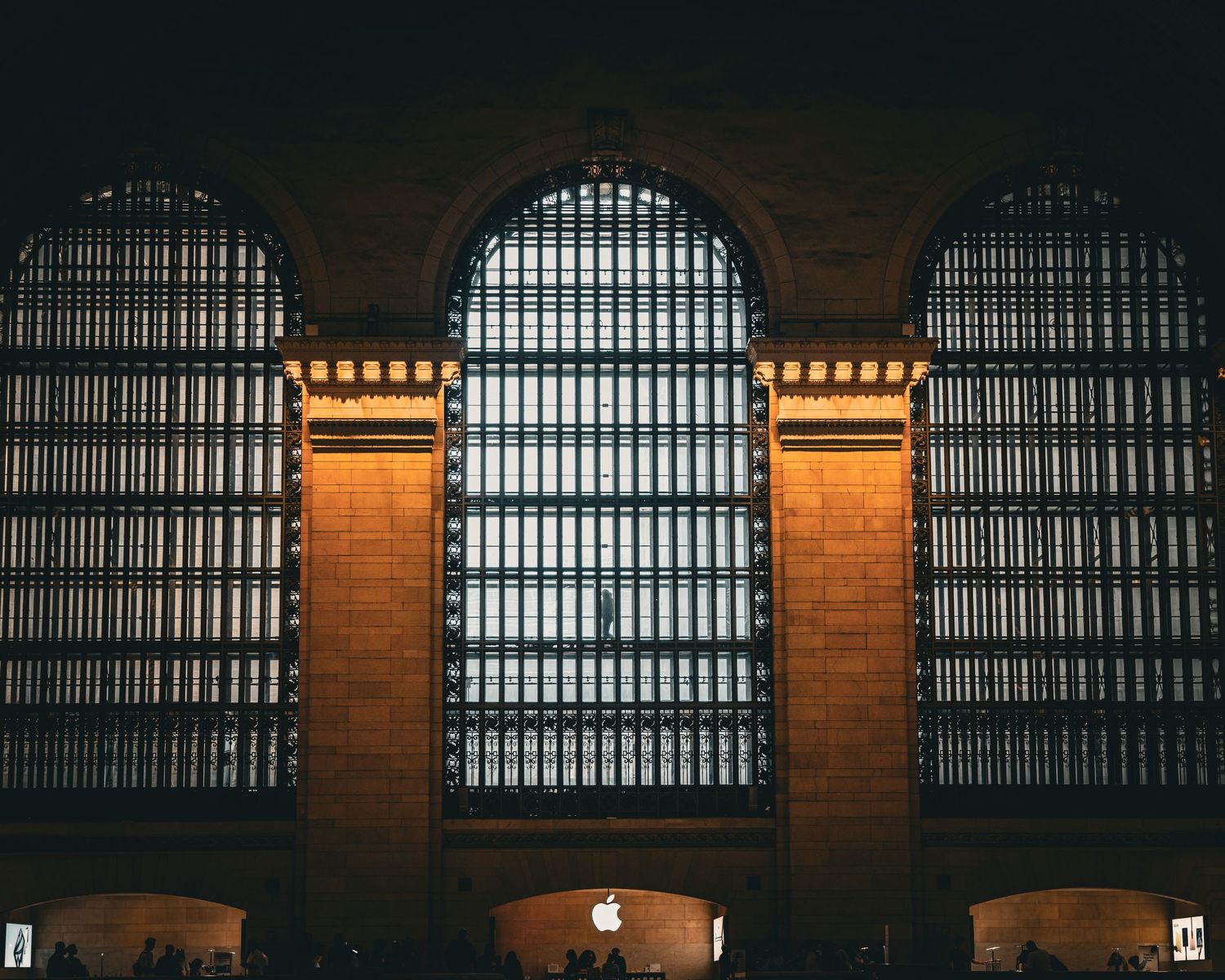 Grand Central Terminal interior featuring three arched windows with golden brick columns and an Apple Store sign below.