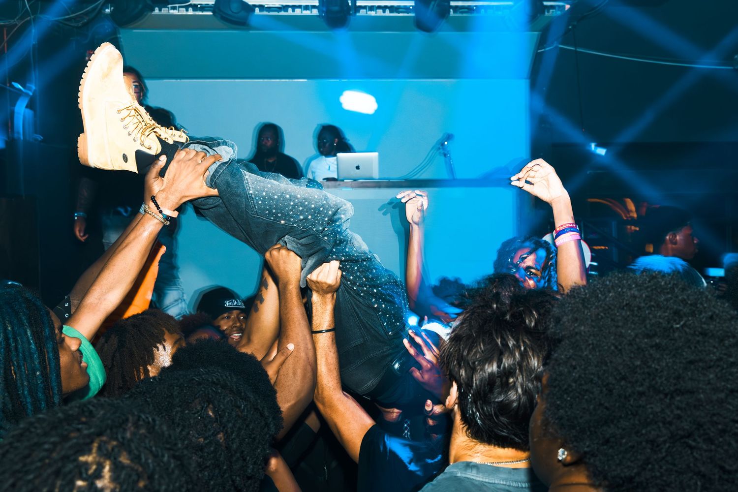 Crowd surfing at a lively nightclub party with blue lights and a DJ in the background.
