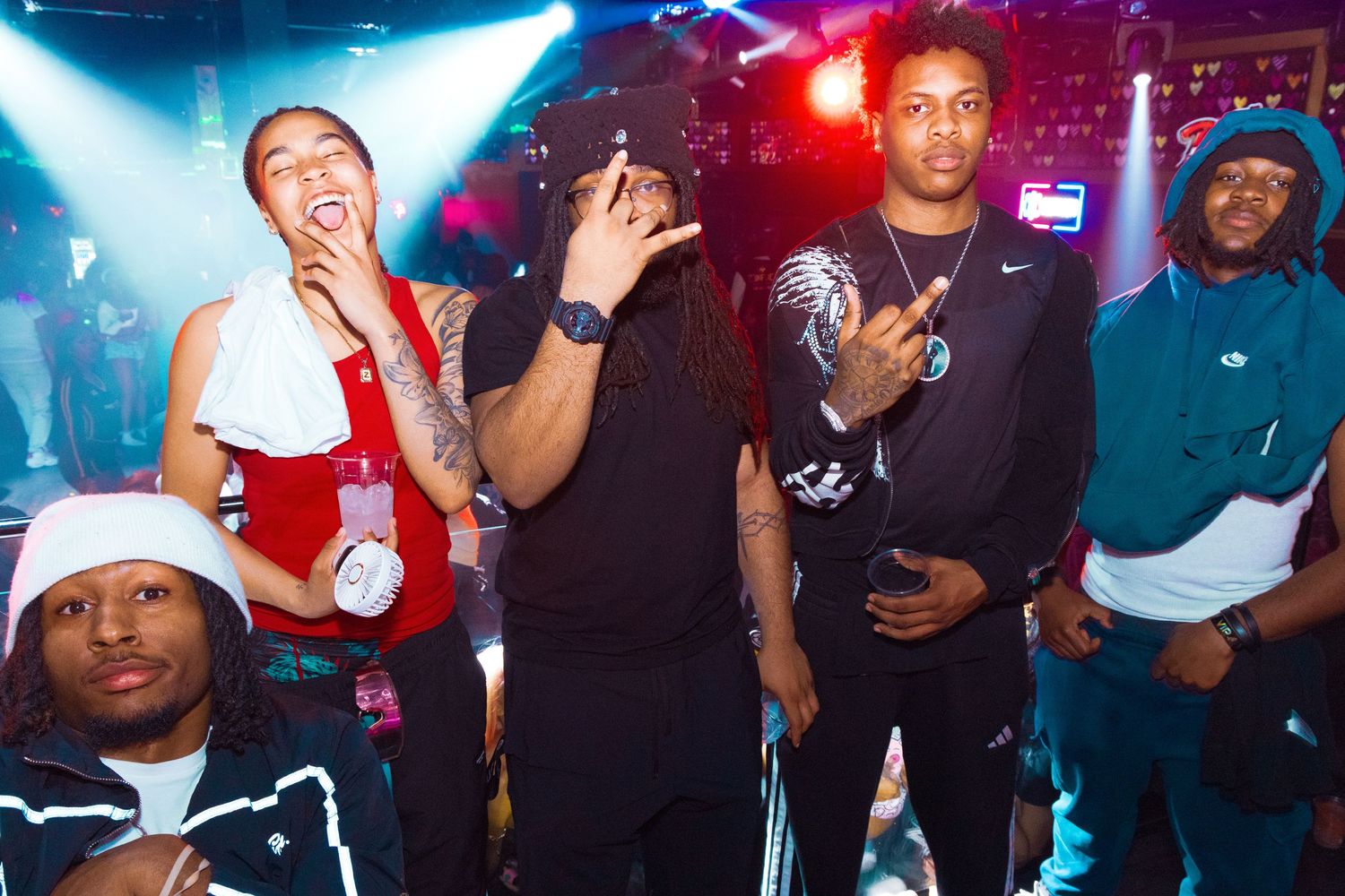 Group of young people posing together at a nightclub party with colorful stage lighting in the background.