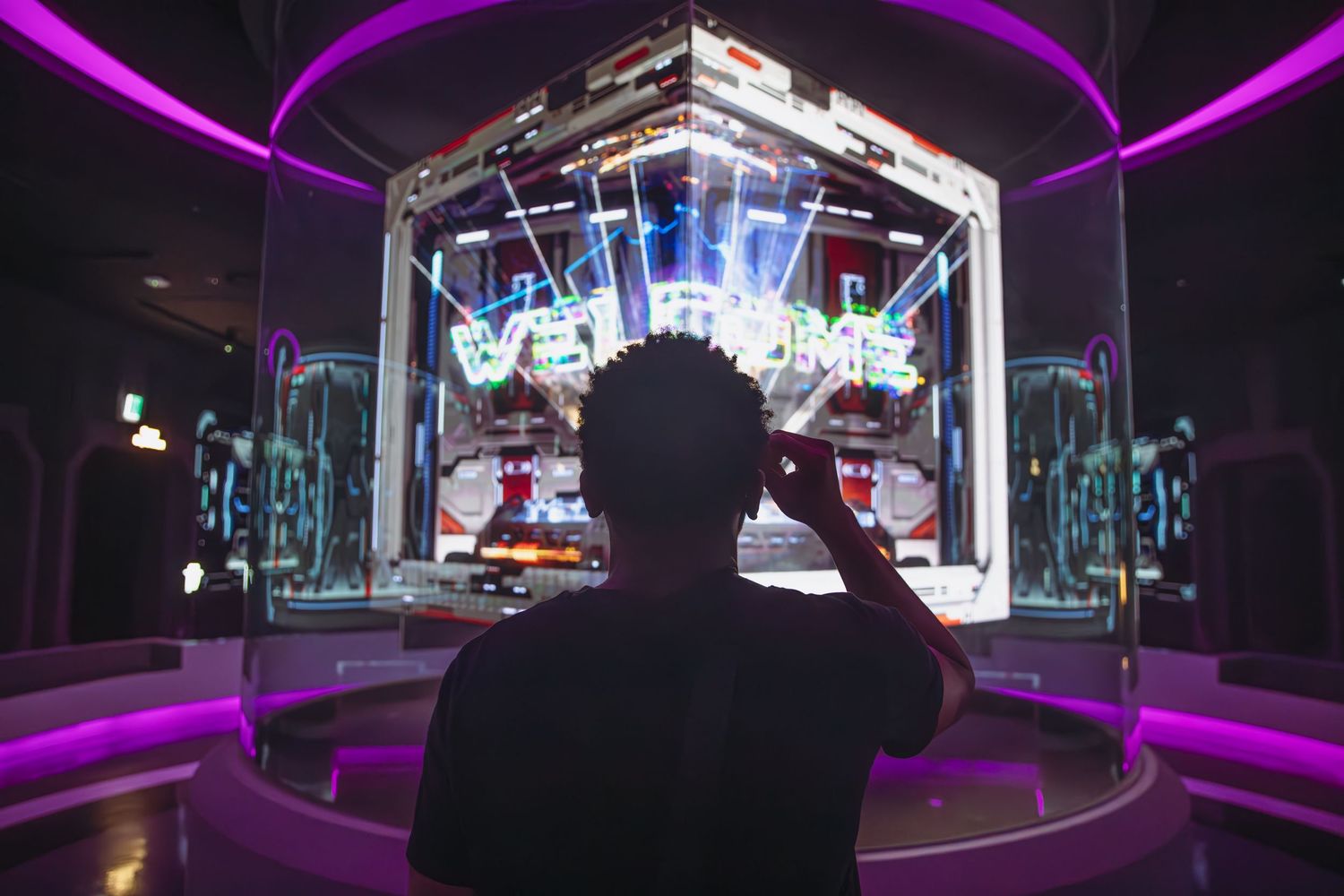 Person viewing a neon welcome sign display in a futuristic purple-lit interactive art exhibit.