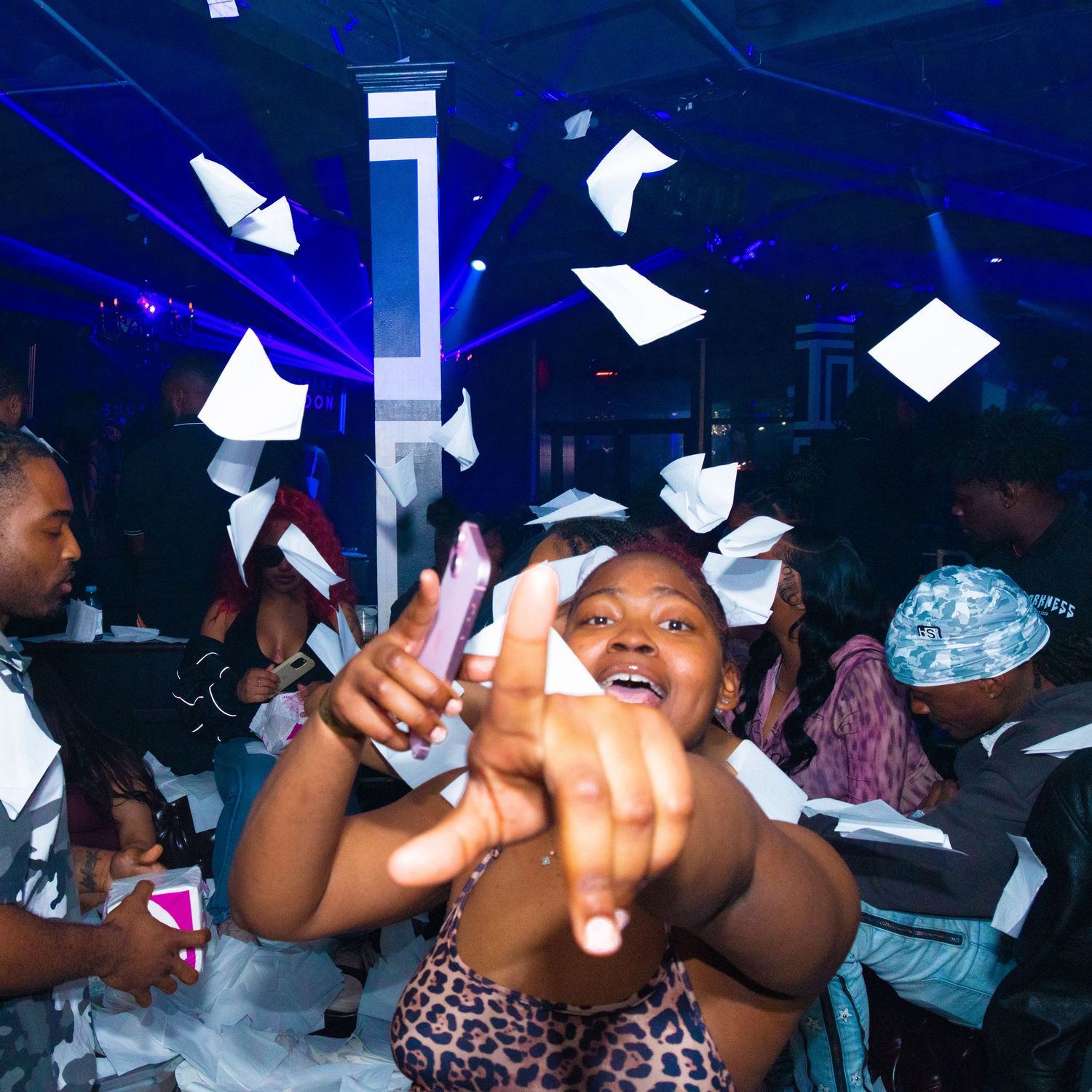 People celebrating at a nightclub party with paper flying in the air under blue lights.