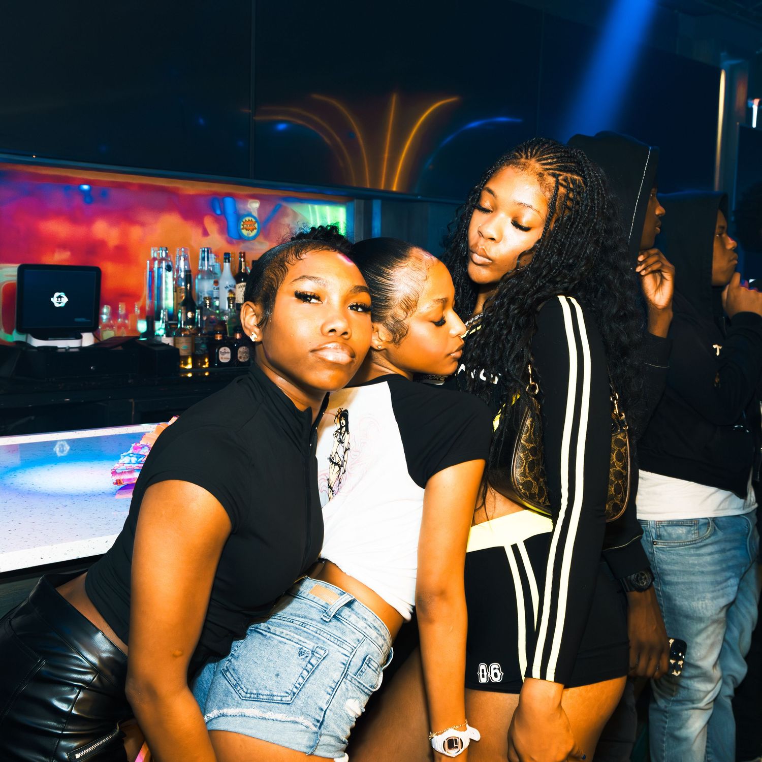 Three young women posing together at a nightclub bar, smiling and enjoying a night out.