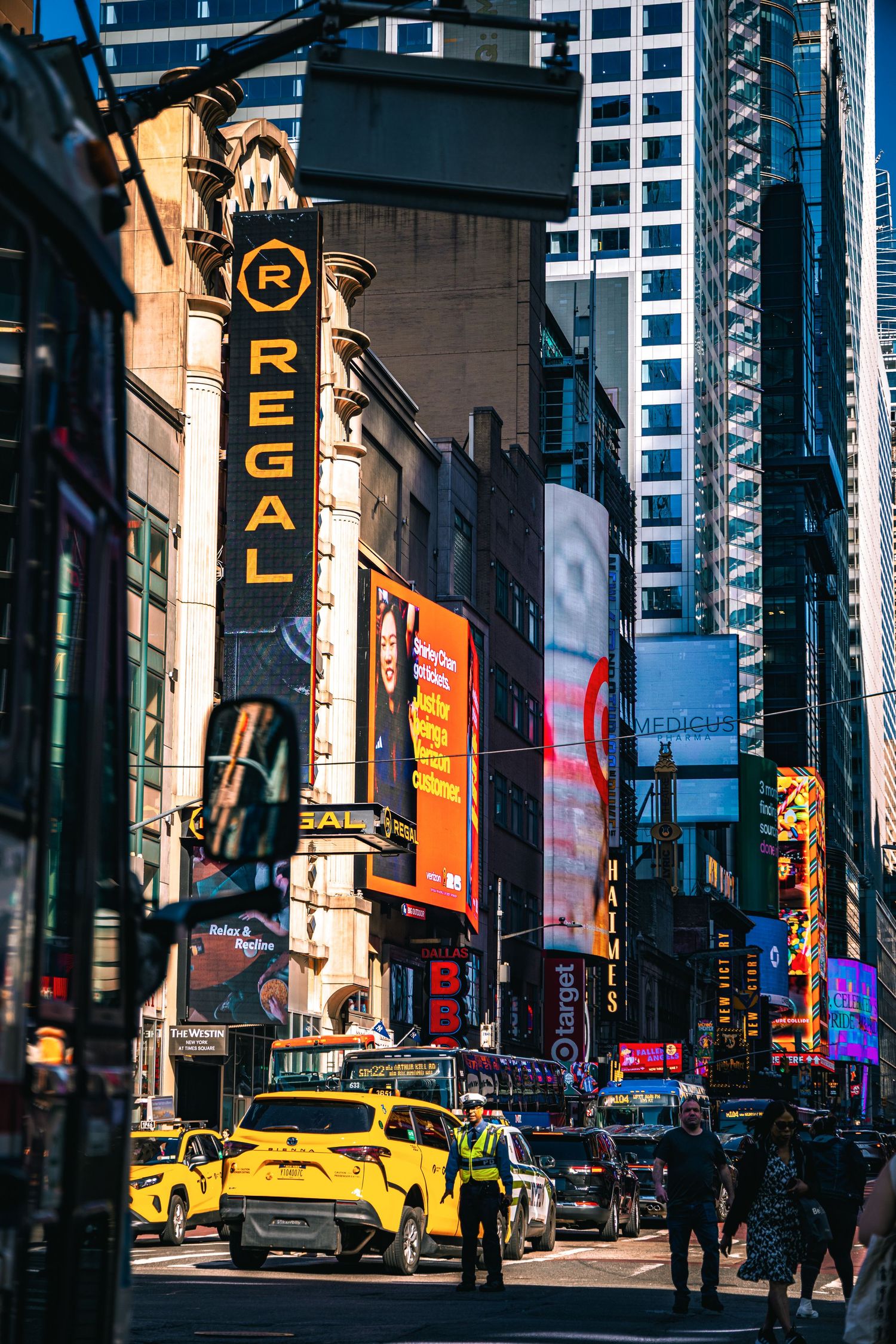 Regal Cinema sign on a bustling Times Square street with yellow taxis, billboards, and a traffic officer in NYC.