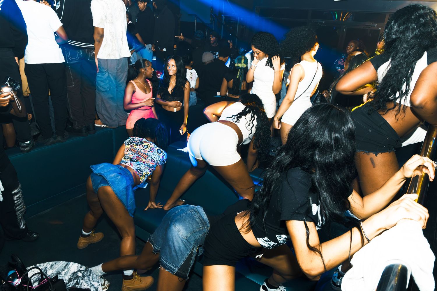 Energetic nightclub dance party with diverse crowd of people dancing under blue lights.