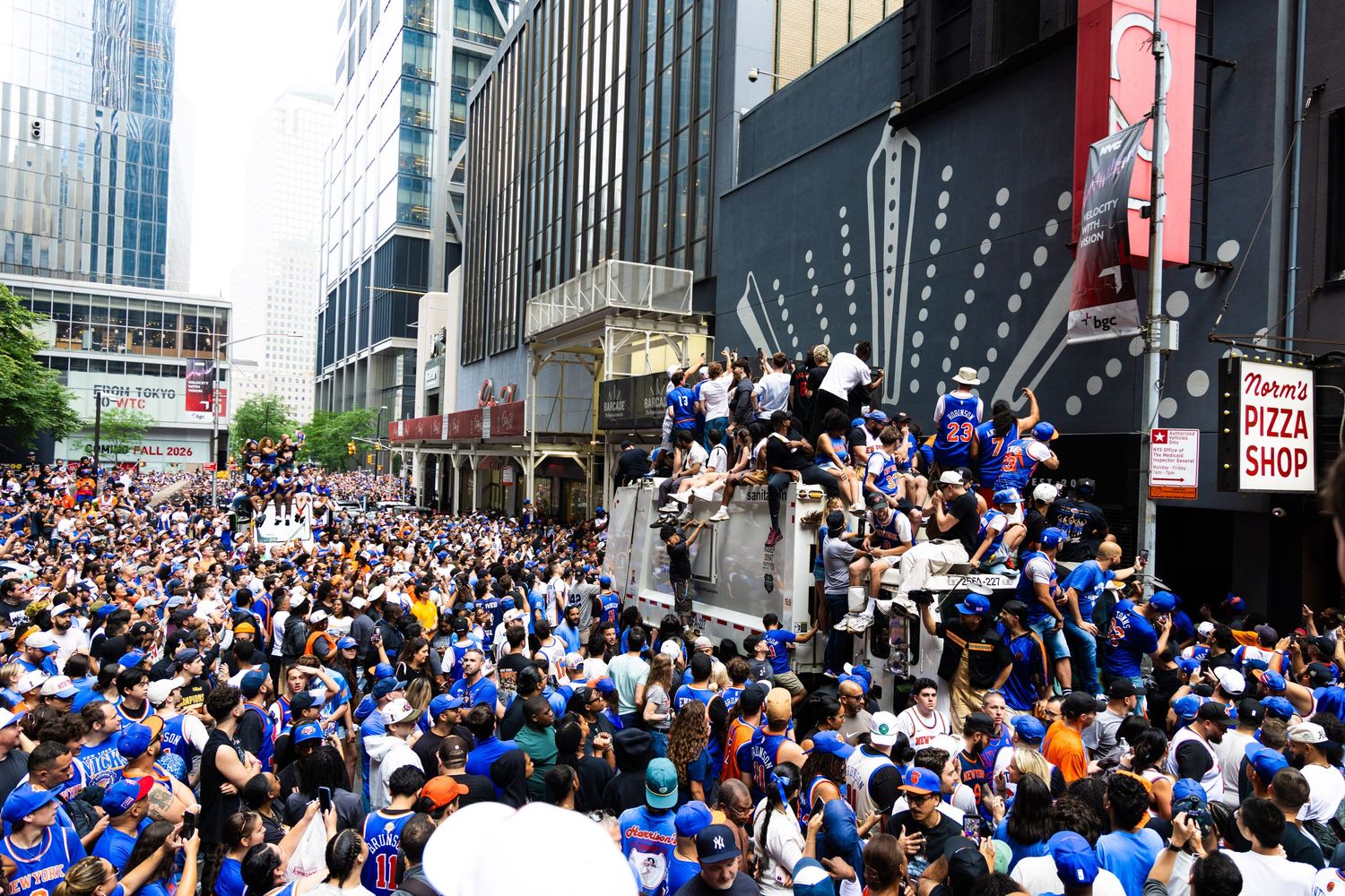 Large crowd of fans in blue jerseys celebrating a championship parade on a busy city street lined with tall buildings.