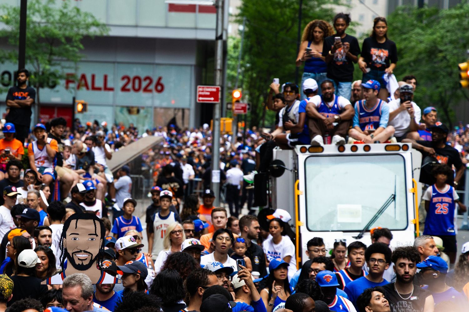 Crowd celebrating a championship parade with players on a truck, fans in blue jerseys lining the streets in 2026.
