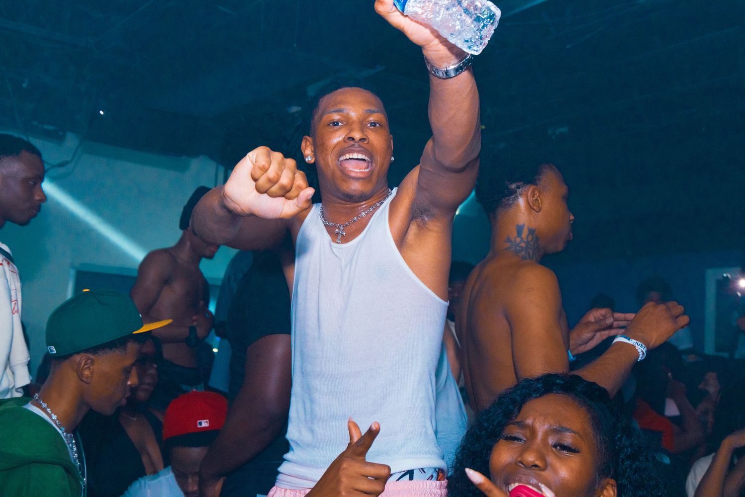 Young man celebrating at a lively nightclub party, raising his fist while being lifted by the crowd.