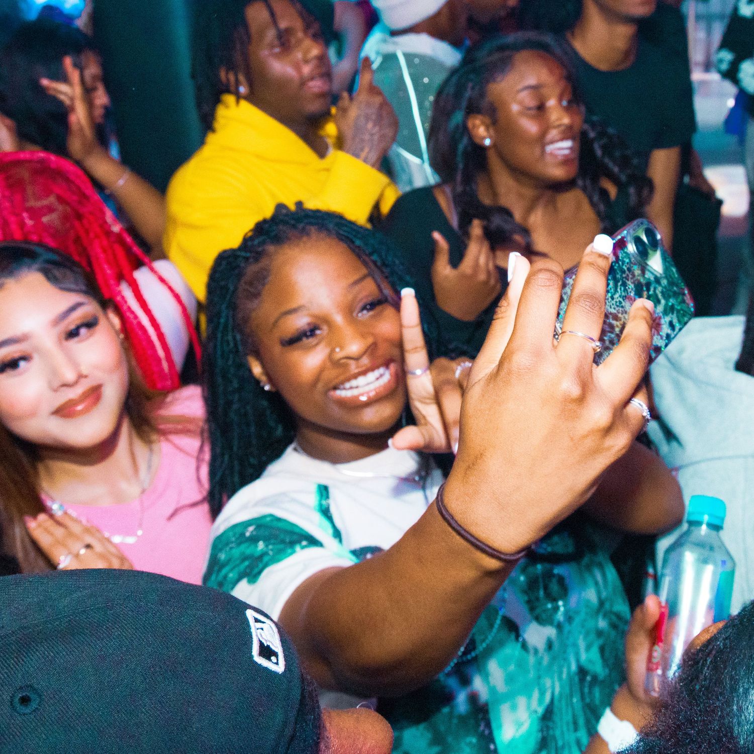 Young woman smiling and taking a selfie at a lively nightclub party with friends in the background.
