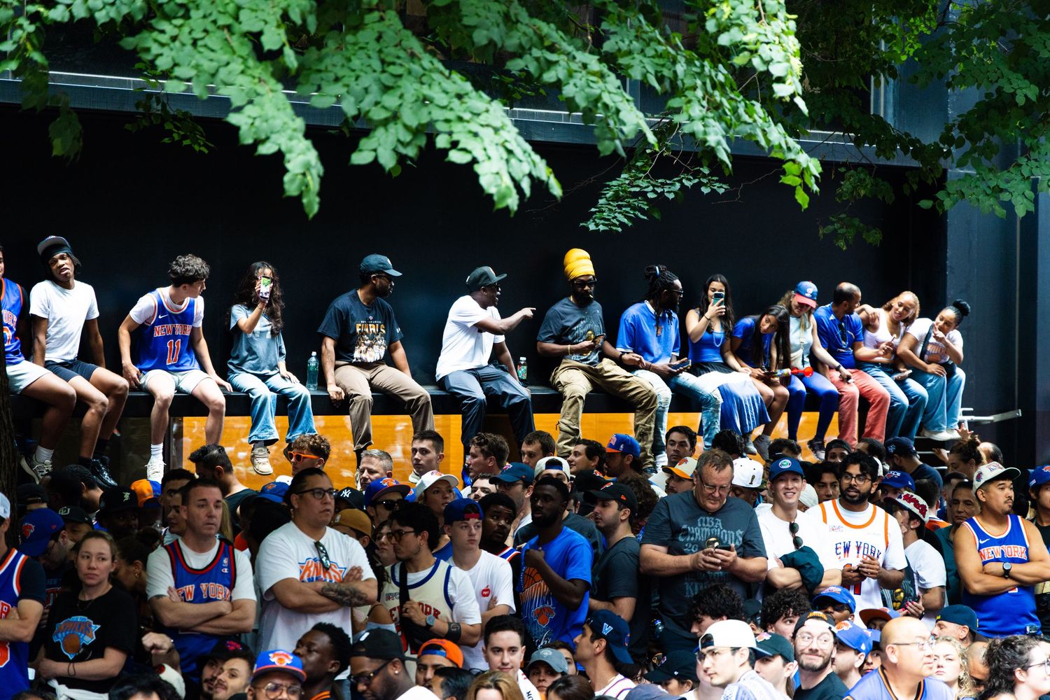 Crowd of New York Knicks fans watching a game outdoors, wearing blue and orange team gear.