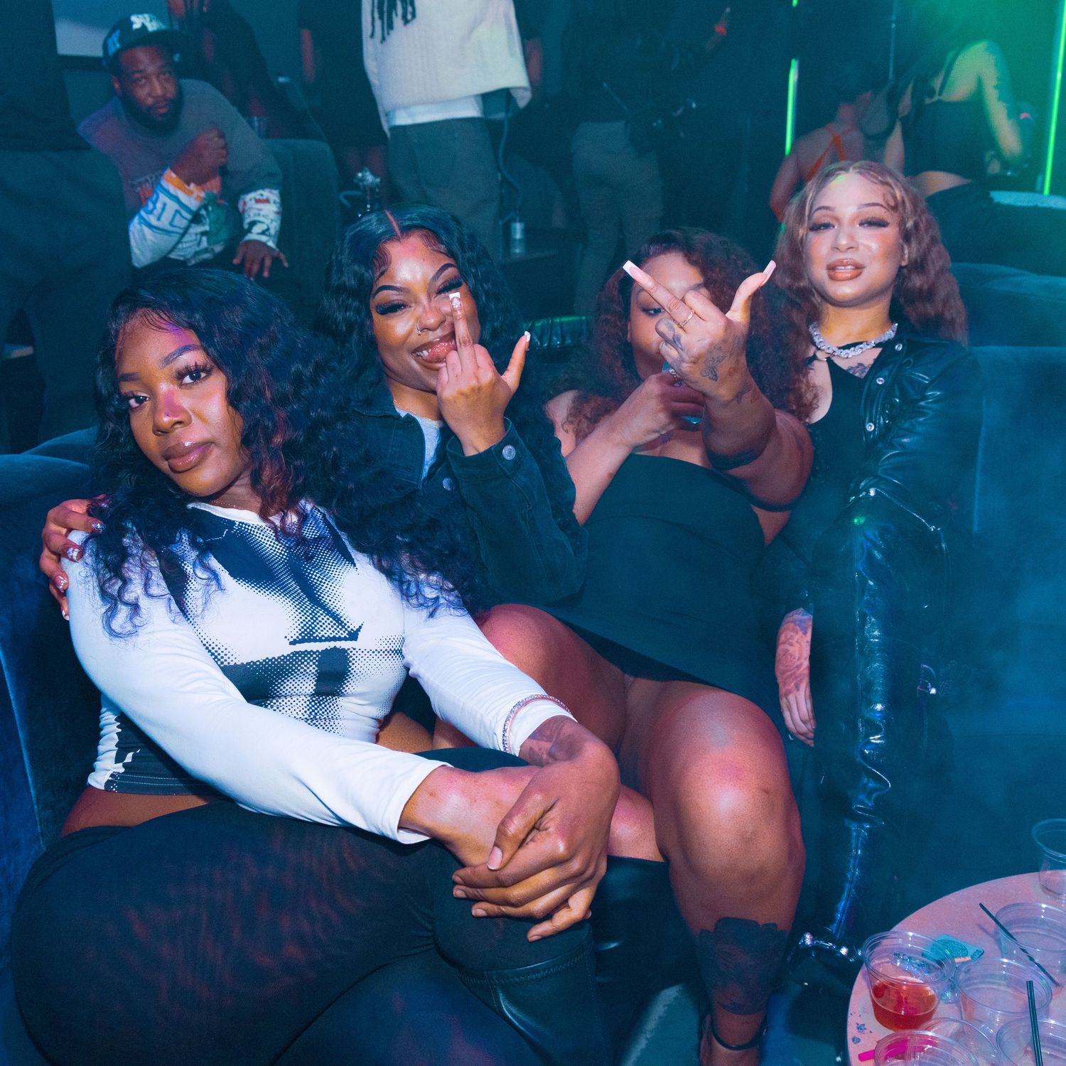 Four women posing together at a nightclub, smiling and making hand gestures in a dimly lit venue.