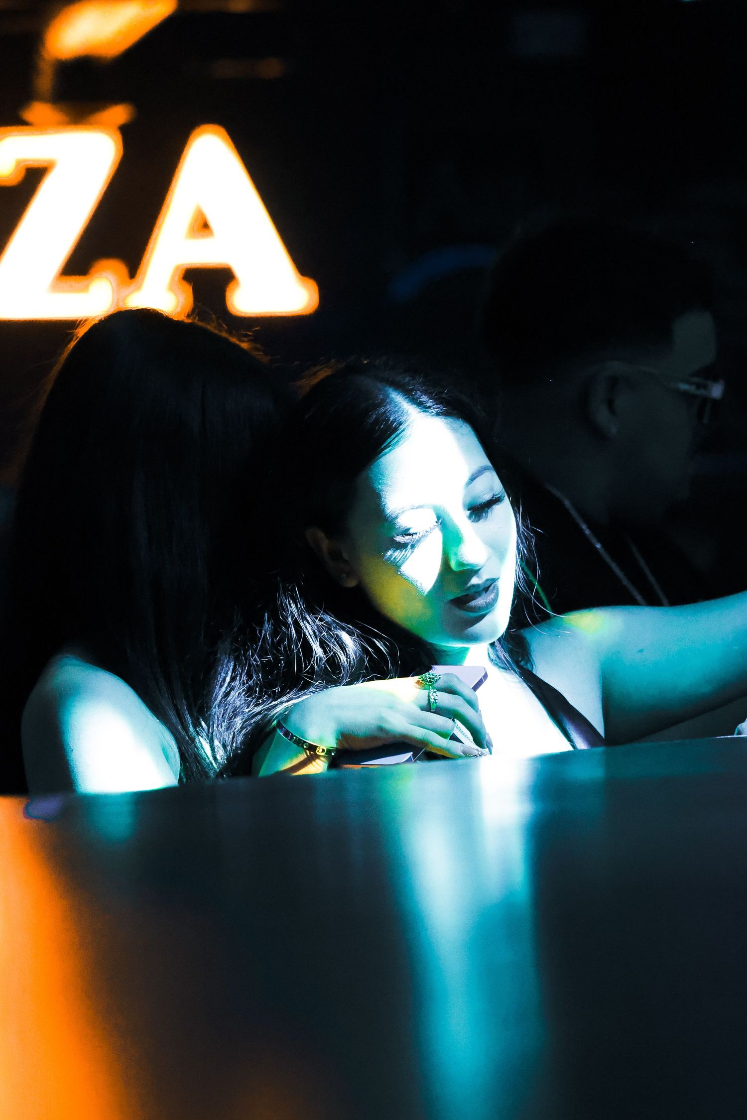 Woman resting her head on a table under blue and orange neon lights in a dark nightclub setting.