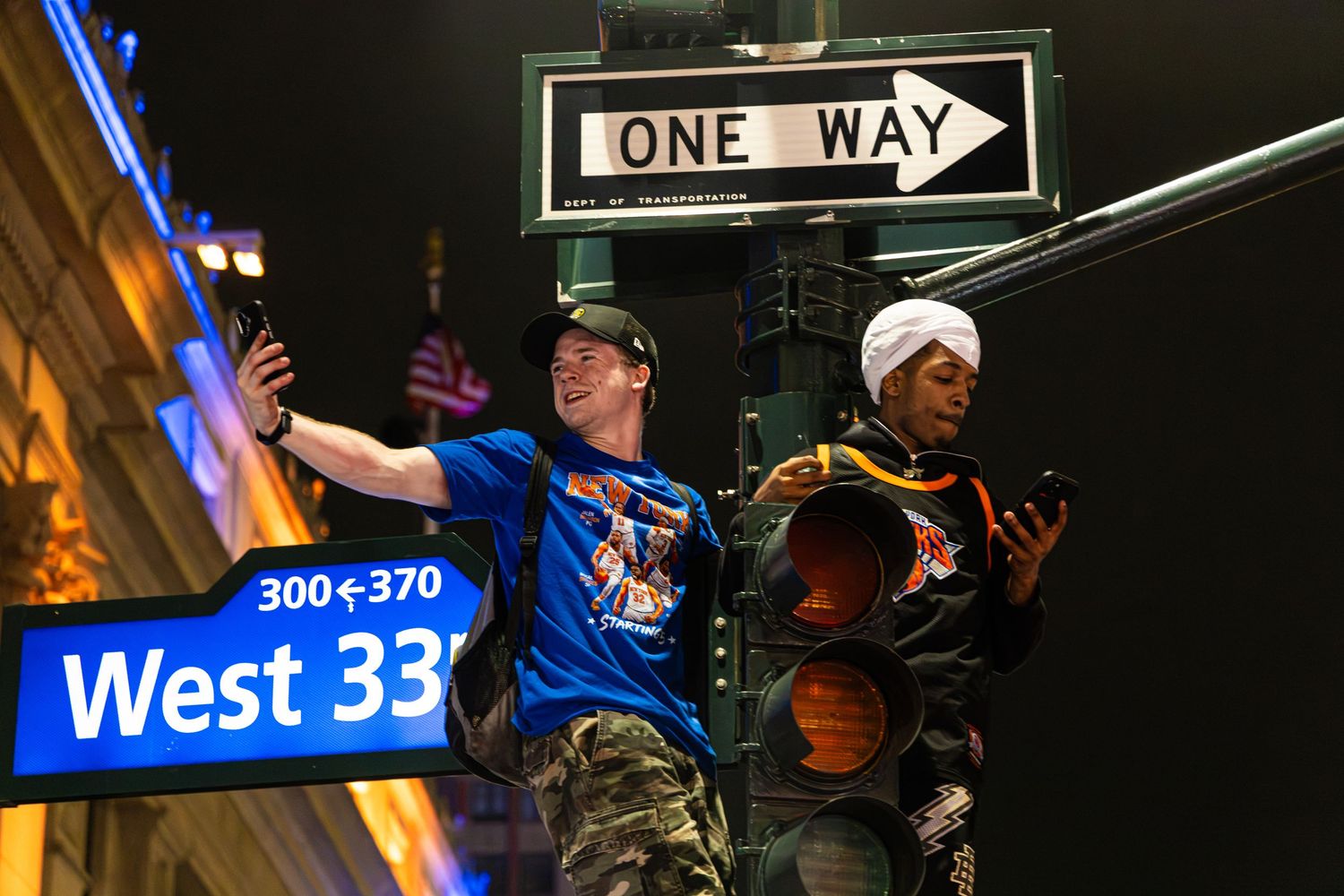 Two people posing under a One Way street sign at West 33rd Street in New York City at night.