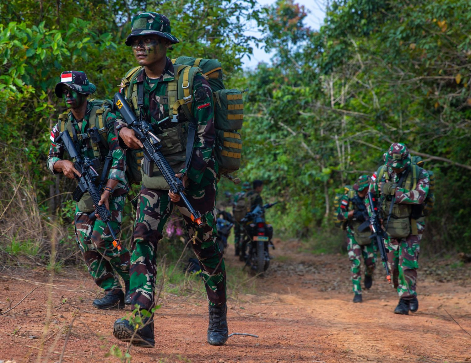 Indonesian soldiers in full combat gear march along a red dirt road during a joint military exercise.