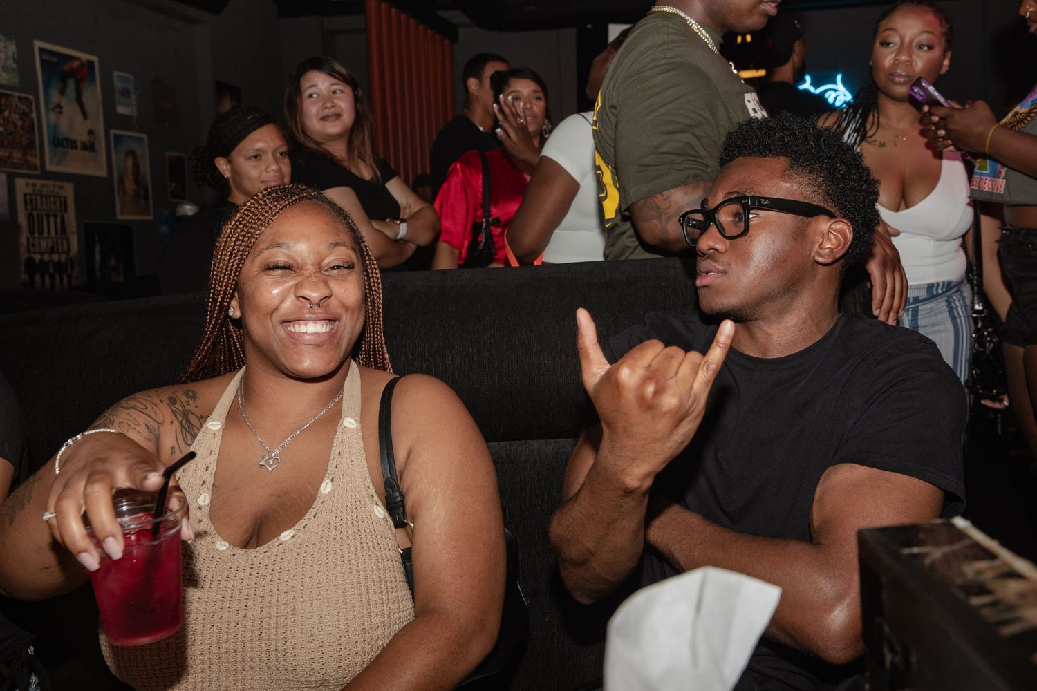 Two friends smiling and posing with drinks at a cozy nightclub lounge.