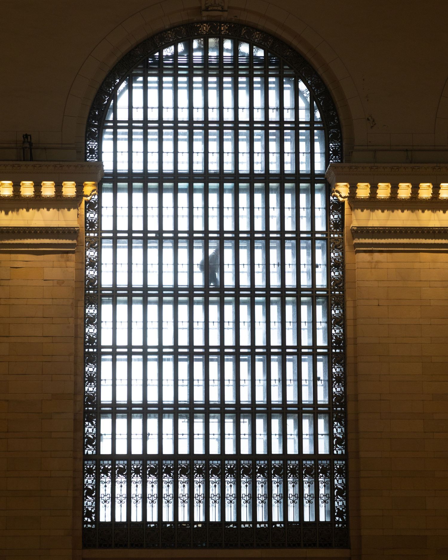Grand Central Terminal's iconic arched window with ornate iron grillwork set in a brick wall, allowing natural light to filter through.