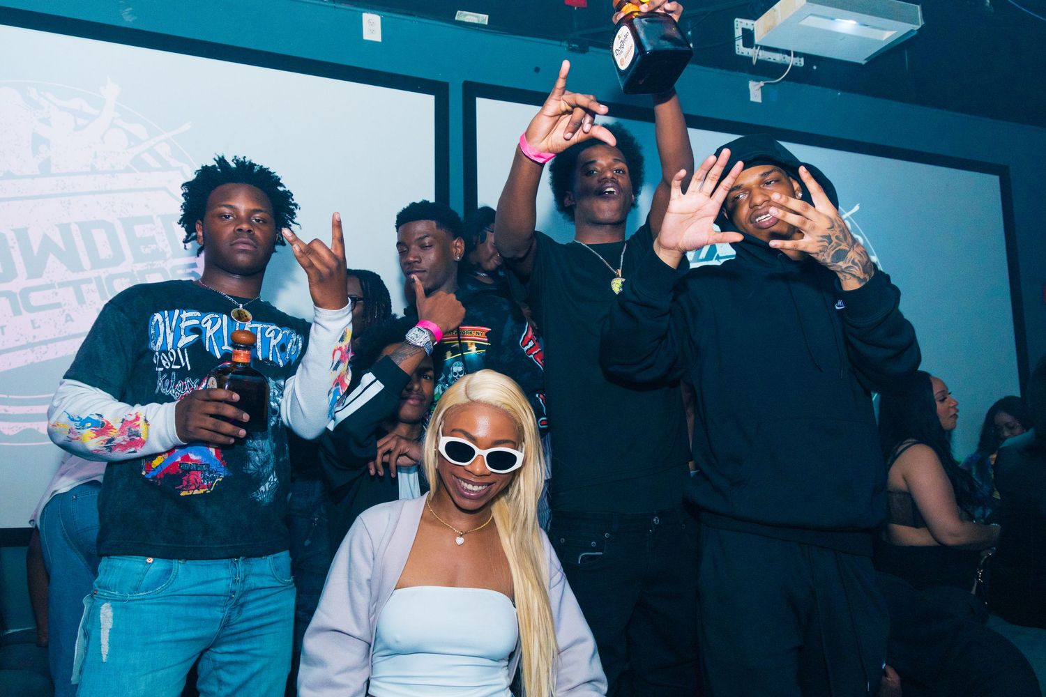 Group of young friends posing and celebrating together at a party event, wearing stylish streetwear outfits.
