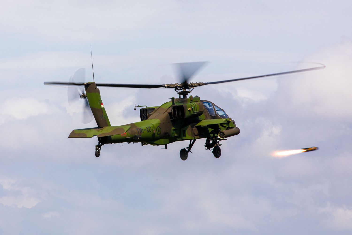 Green camouflage Apache helicopter launching a missile during a military training exercise.