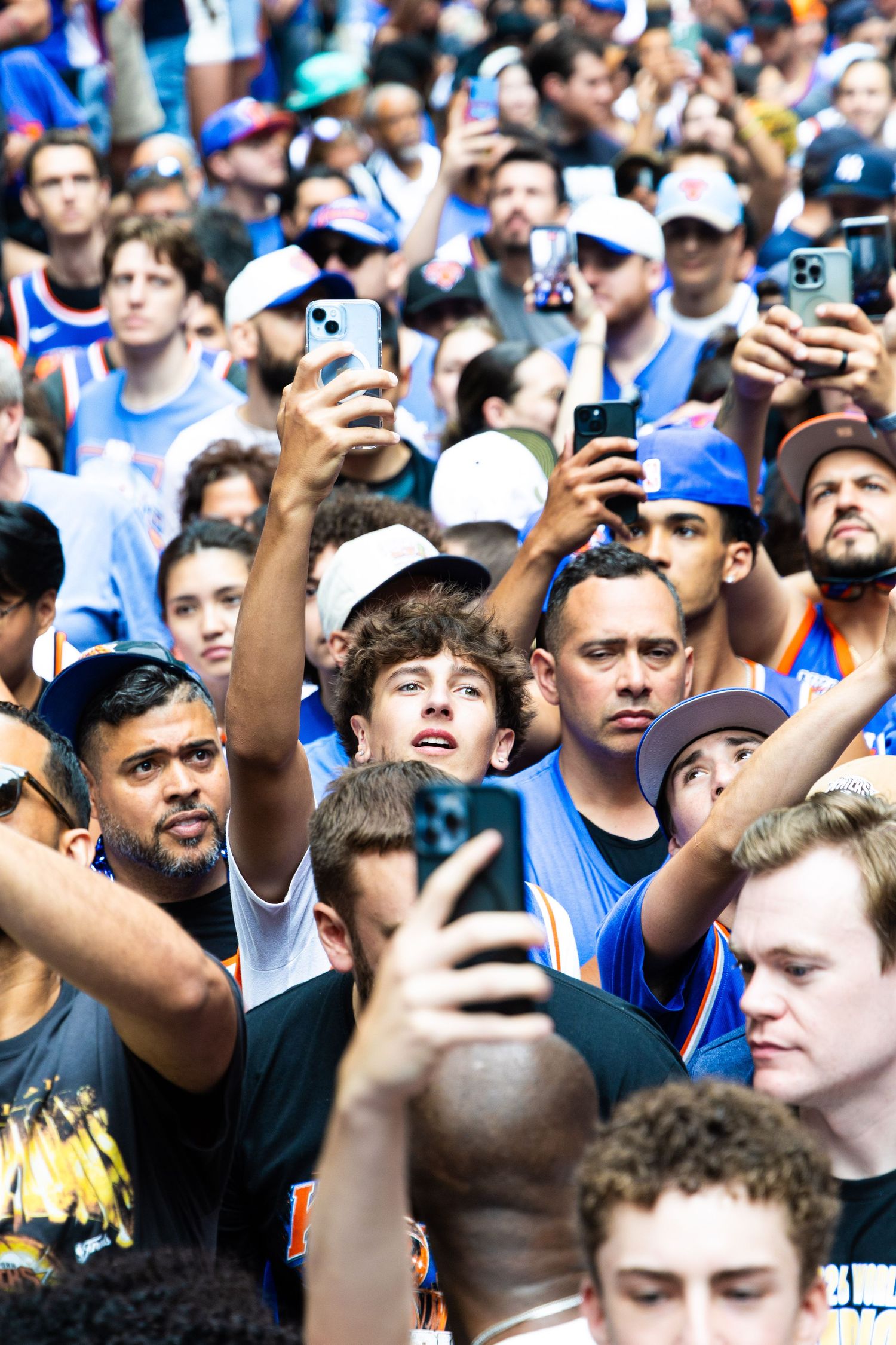 Large crowd of New York Knicks fans holding up smartphones at an outdoor rally event.