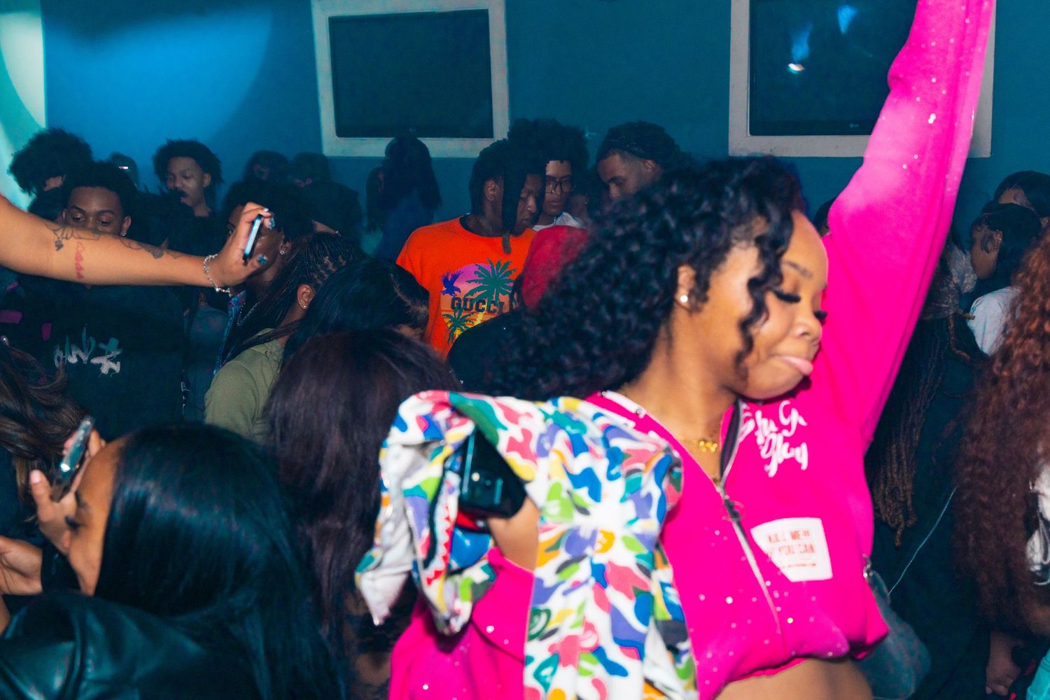 Women in colorful outfits dancing at a vibrant nightclub party with a lively crowd in the background.