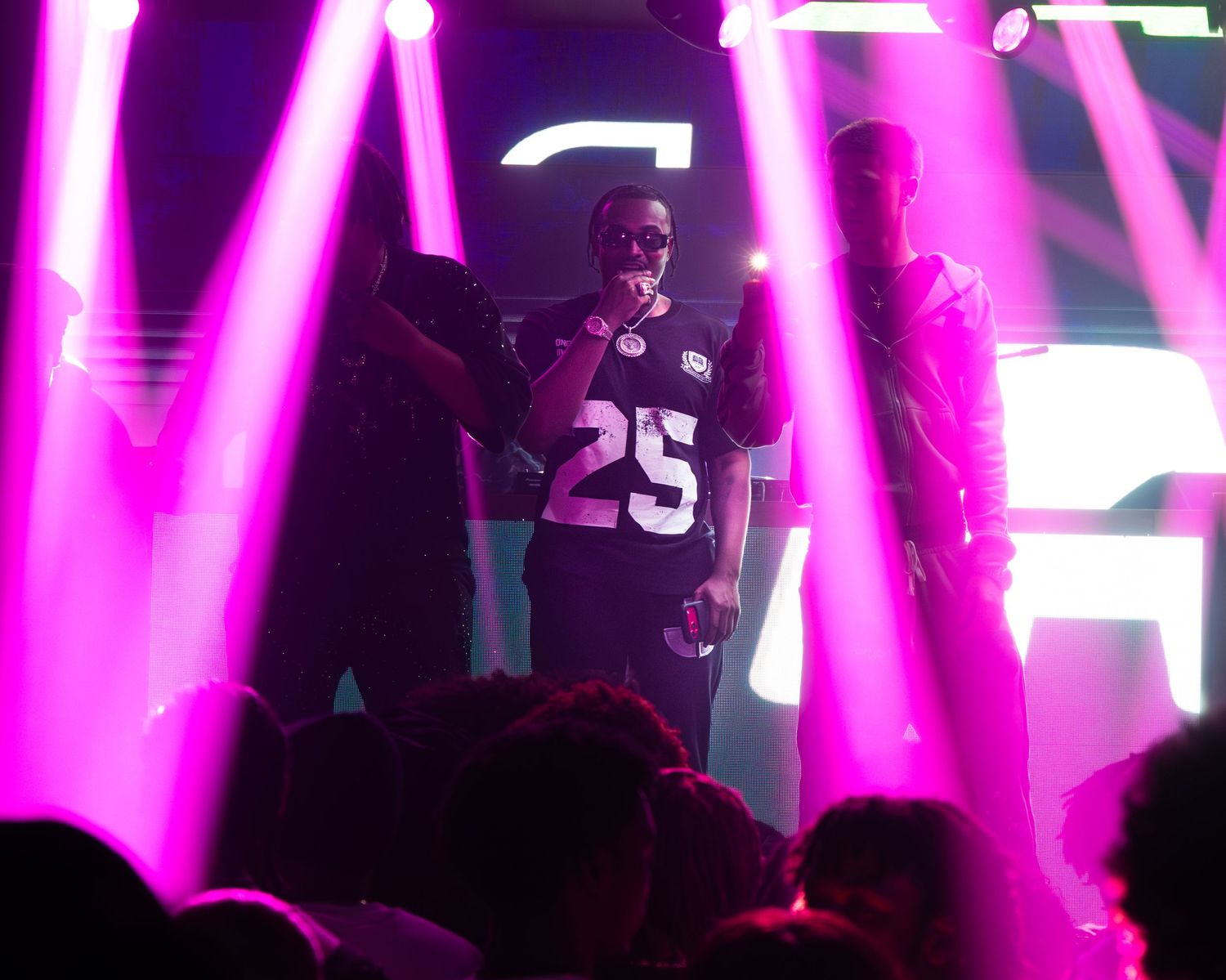 Performer in jersey number 25 on stage with vibrant pink and purple lighting at a nightclub event.