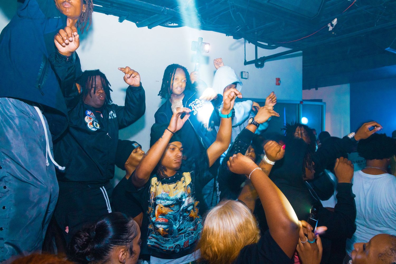 Group of young people dancing and celebrating at a lively indoor party with blue lighting.