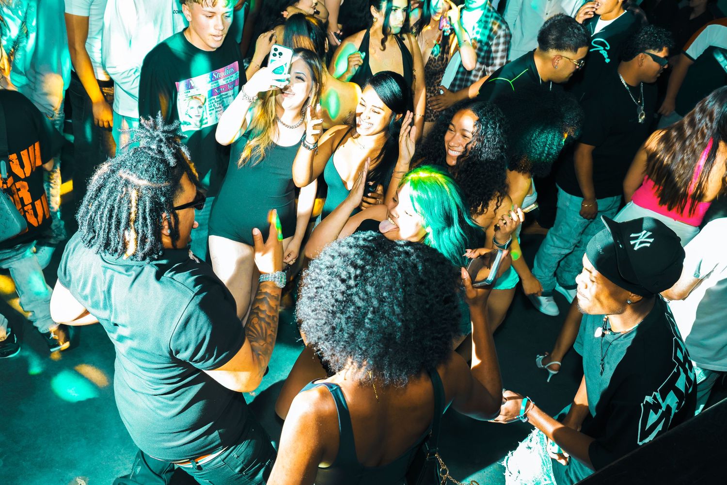 Diverse group of people dancing and socializing at a vibrant nightclub party with green lighting.