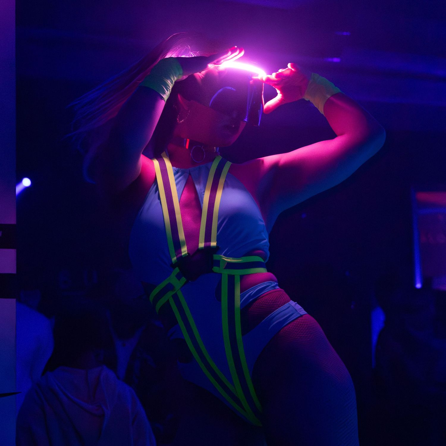Woman in neon glow-in-the-dark outfit dancing under UV black lights at a nightclub party.