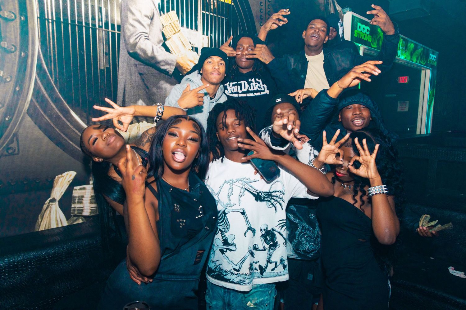 Group of friends posing and having fun at a nightclub party, making hand gestures and smiling.