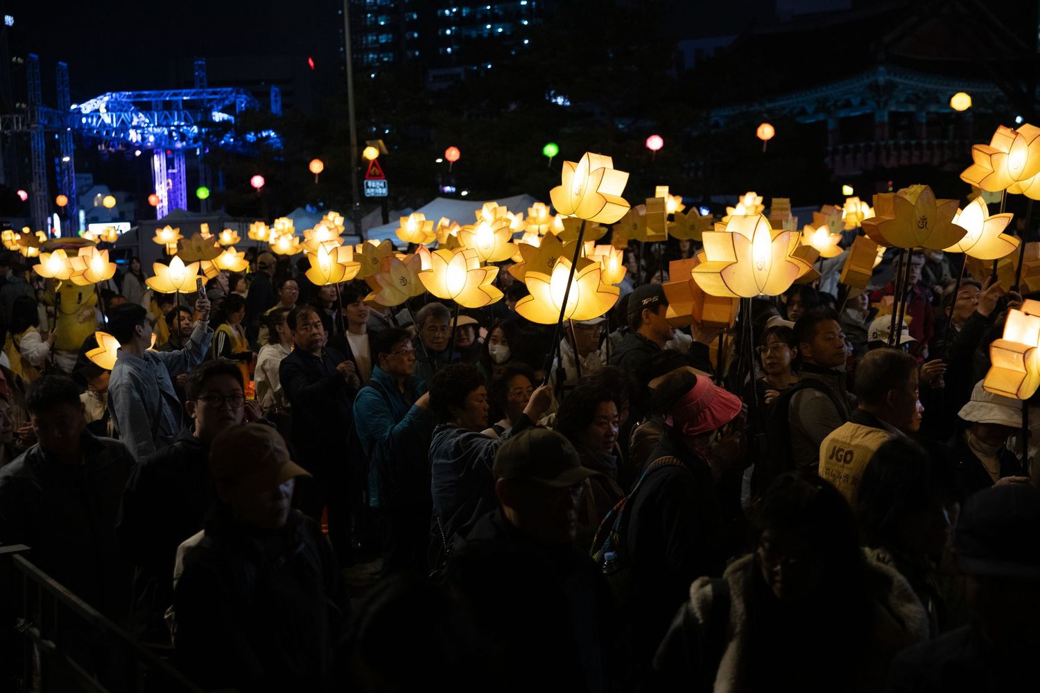 Crowd holding illuminated lotus lanterns during a Buddhist lantern festival at night.