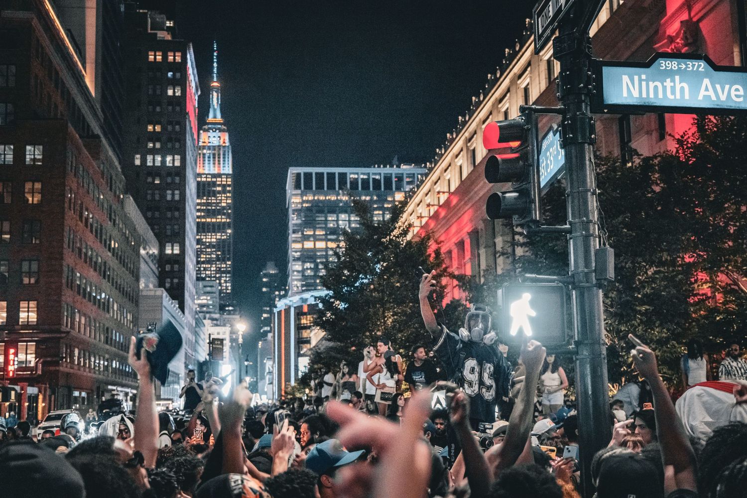 Crowd celebrating at night on Ninth Ave in NYC with Empire State Building lit up in background.