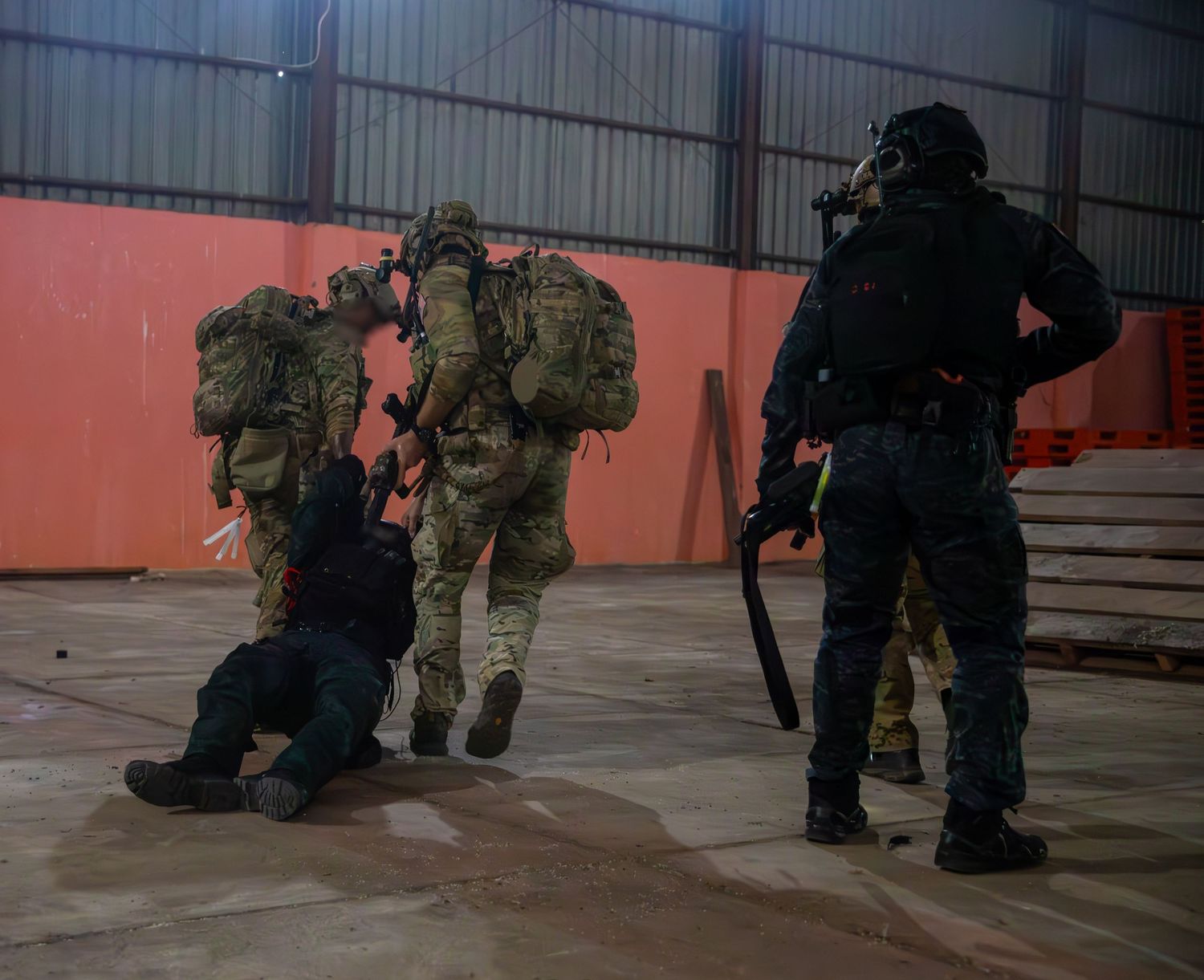 Special operations soldiers with tactical gear detaining a suspect during indoor military training.