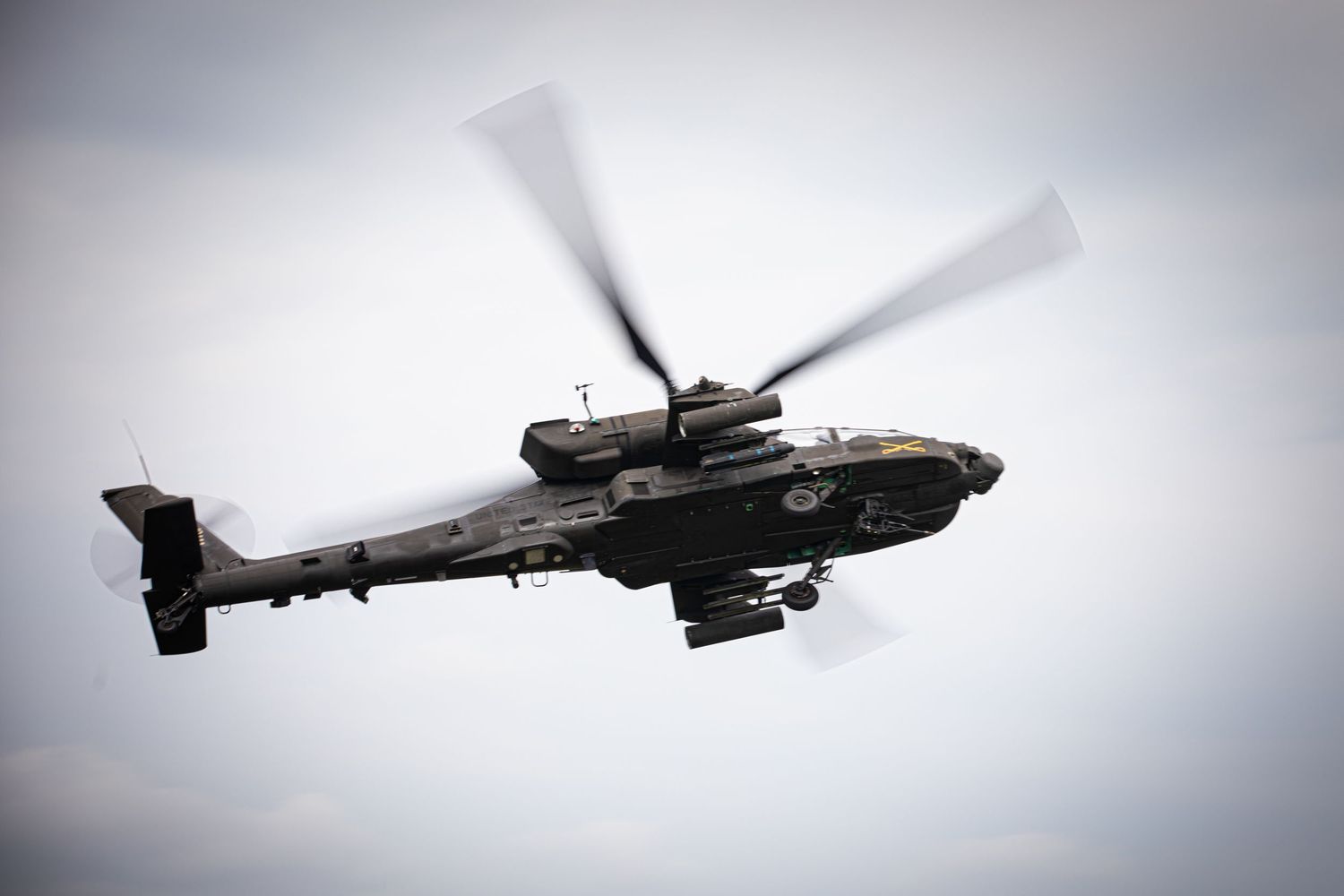 AH-64 Apache attack helicopter flying against overcast sky during military operation.