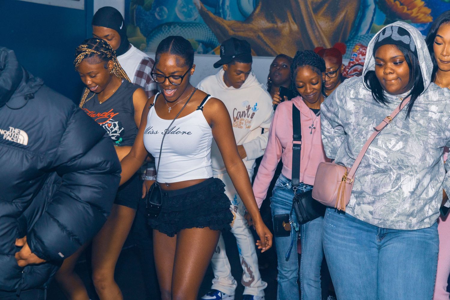 Group of young people dancing and socializing at an indoor party event with colorful wall art in background.